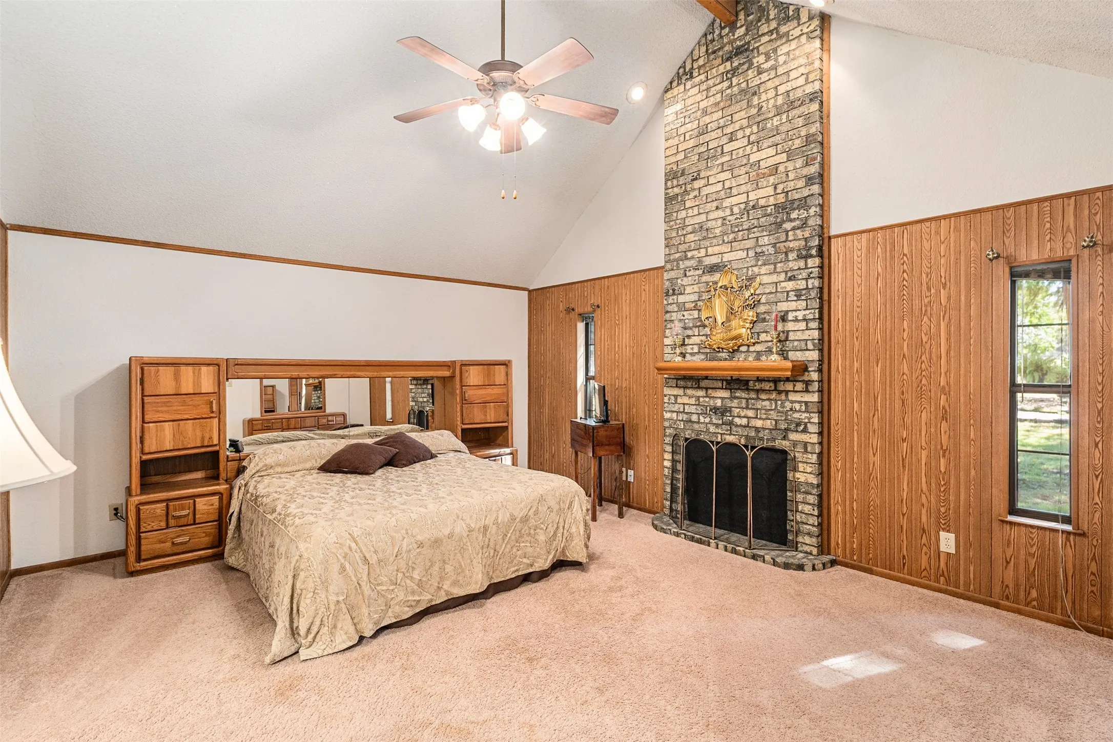 Bedroom with wood walls, carpet flooring, high vaulted ceiling, a fireplace, and ceiling fan