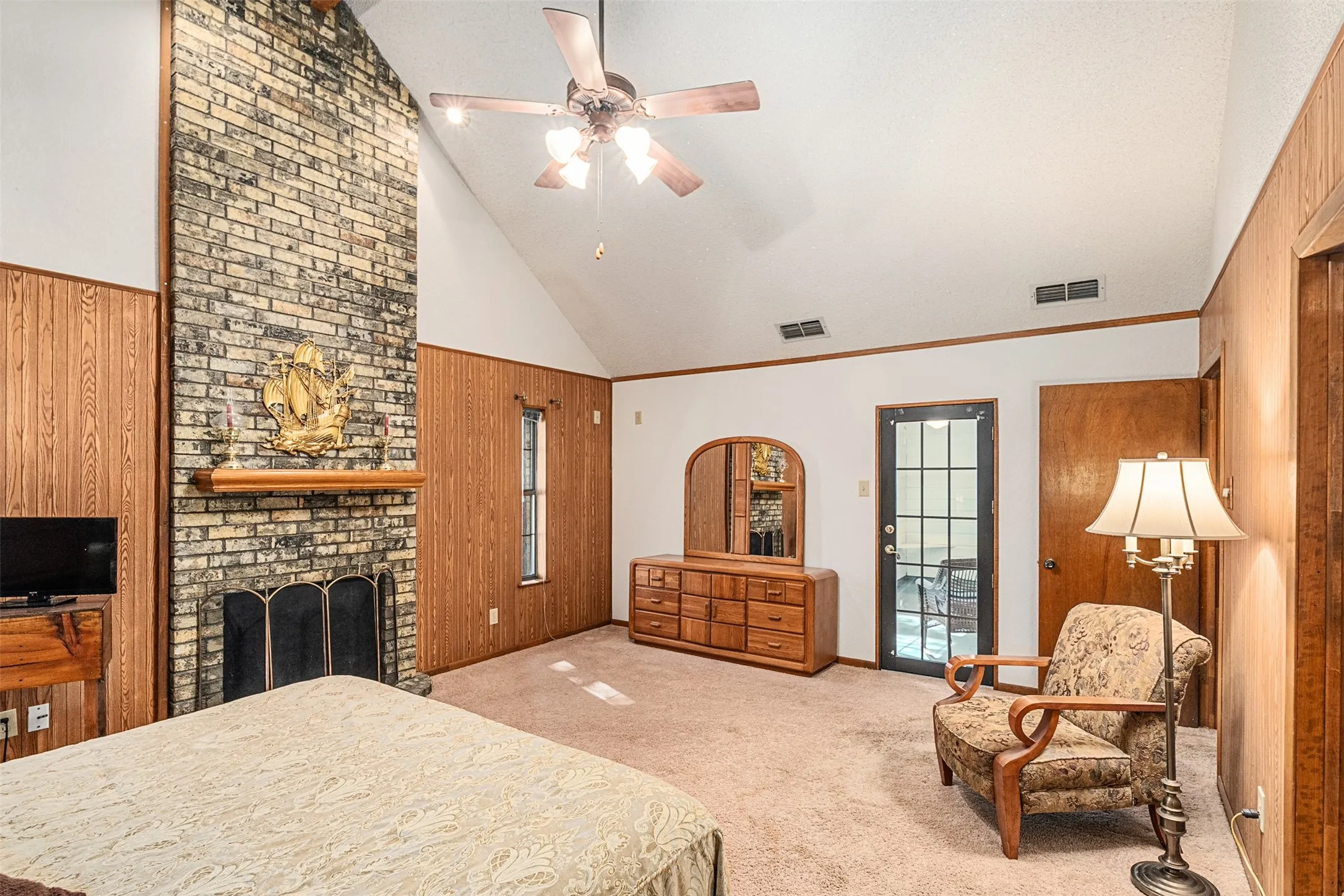 Carpeted bedroom featuring wooden walls, a ceiling fan, high vaulted ceiling, and a fireplace
