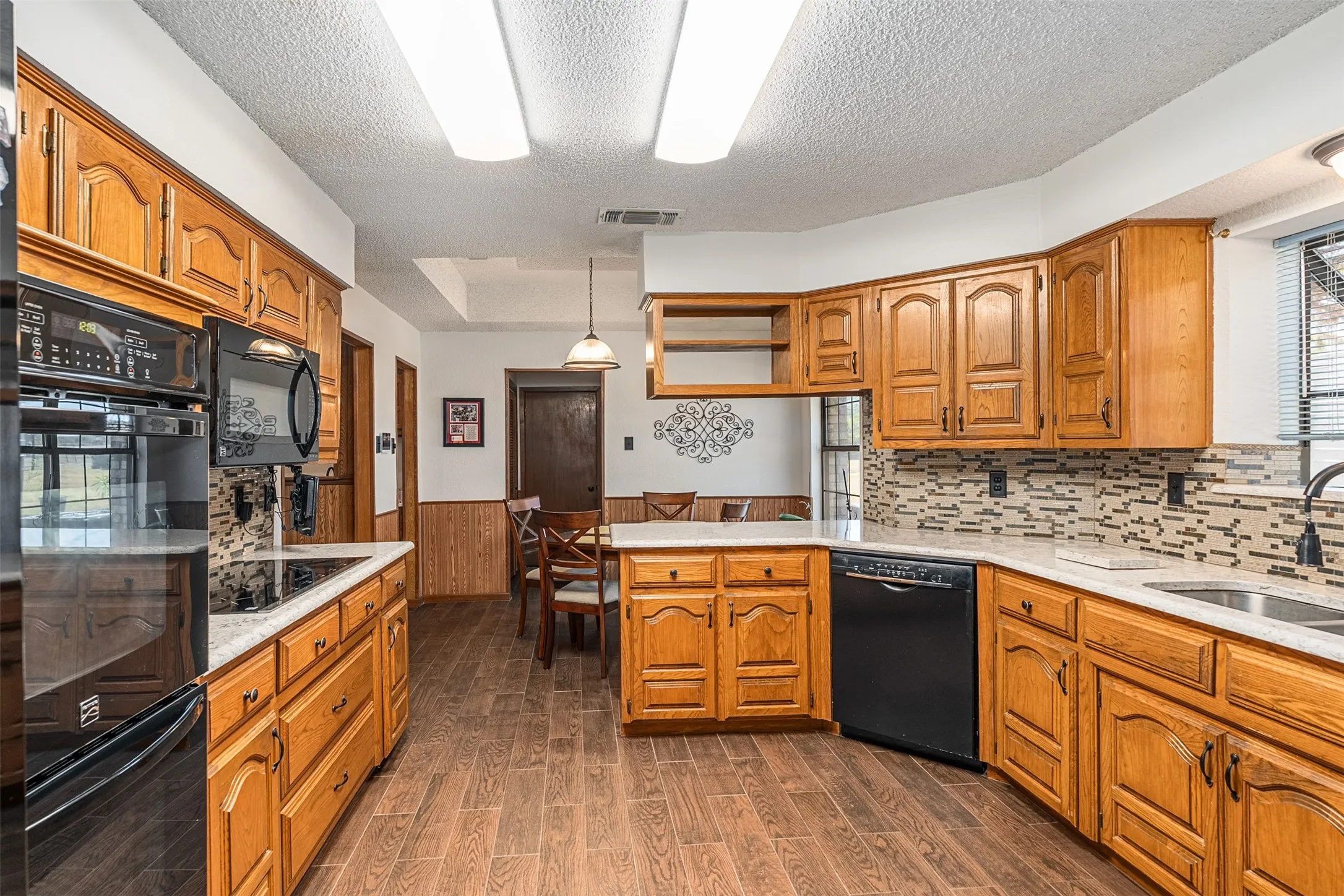 Kitchen featuring light stone counters, a peninsula, black appliances, brown cabinets, and hanging light fixtures