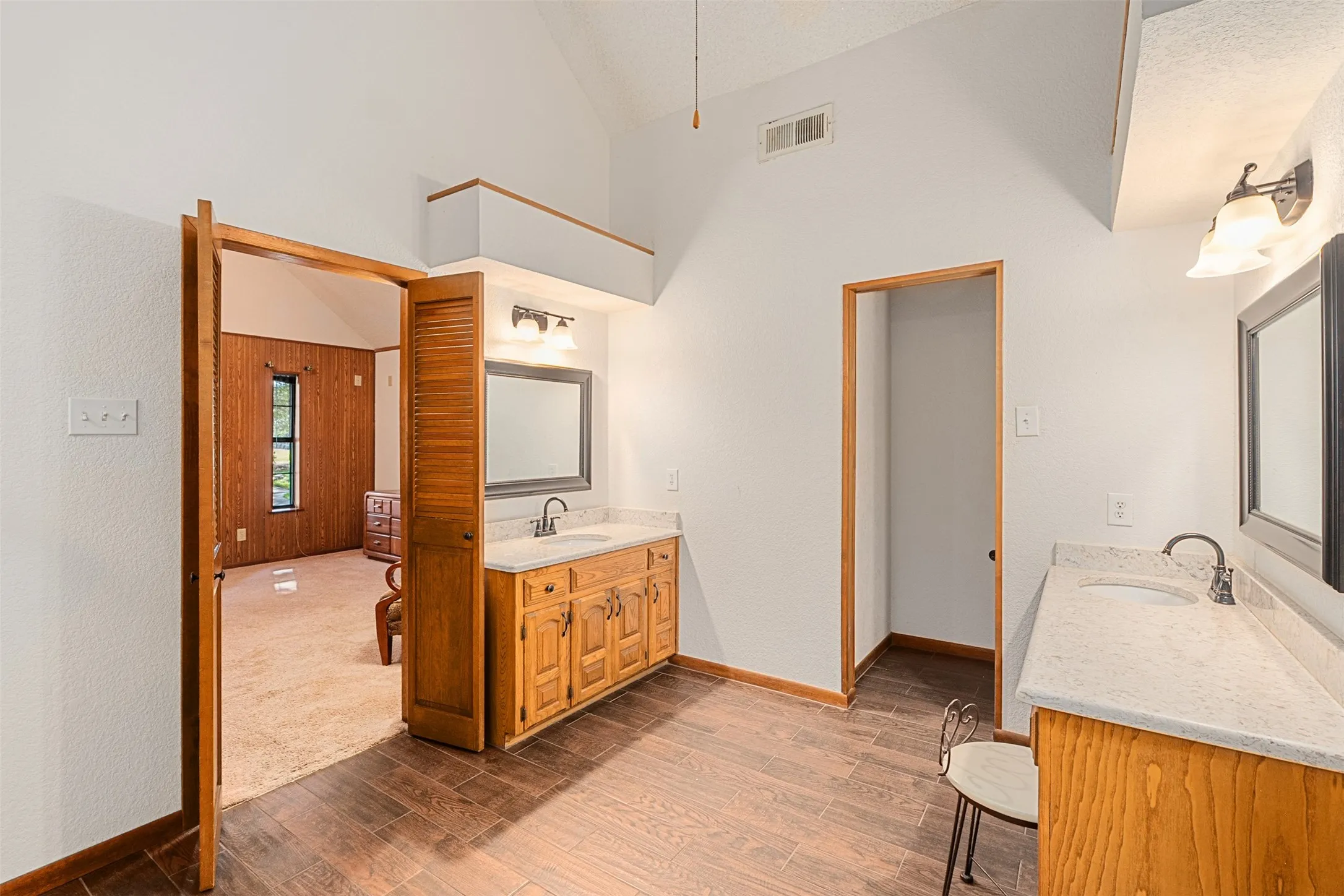Primary full bath with dark wood finished floors, two vanities, and high vaulted ceiling