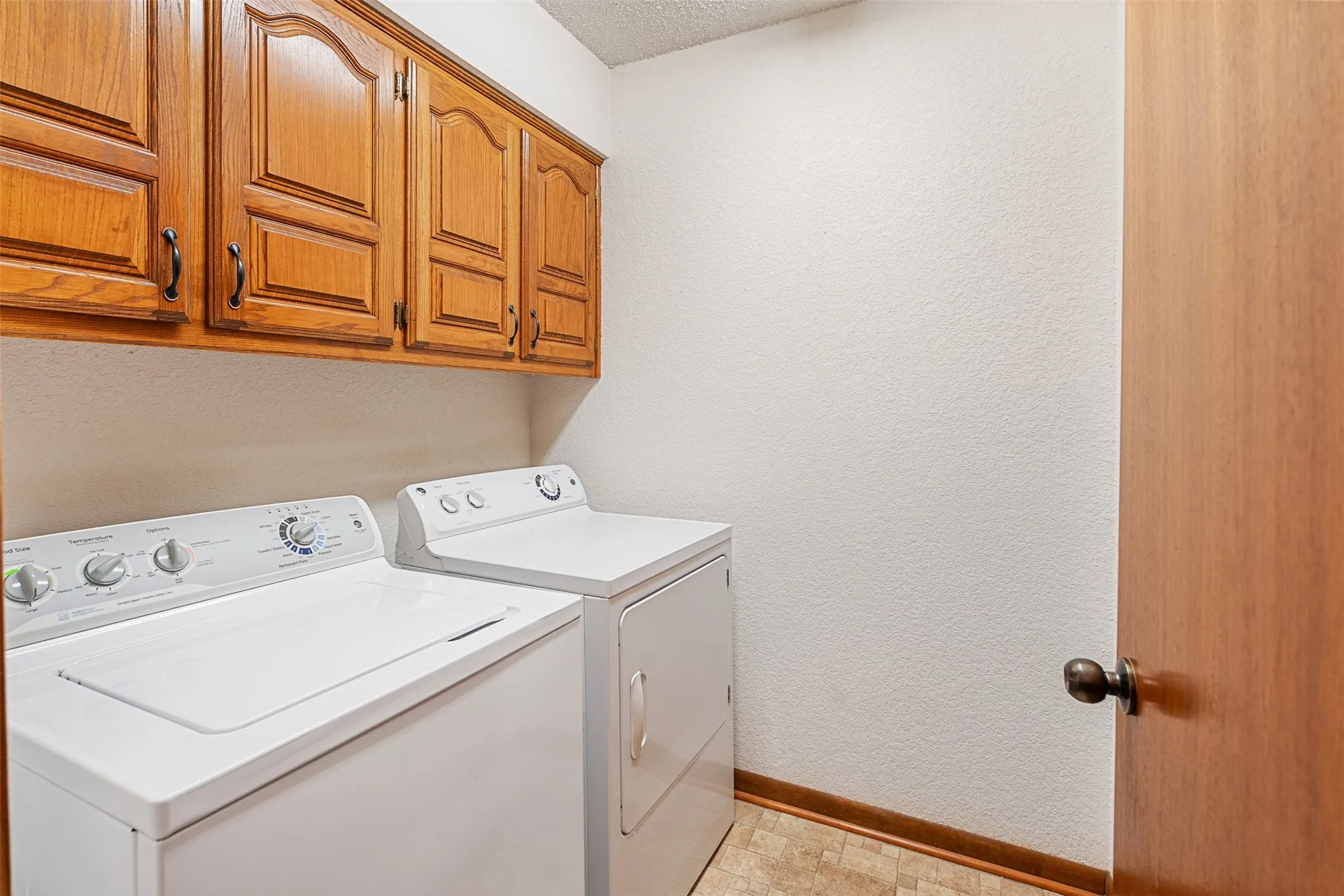 Laundry room featuring a textured wall, washing machine and clothes dryer, cabinet space, and a textured ceiling