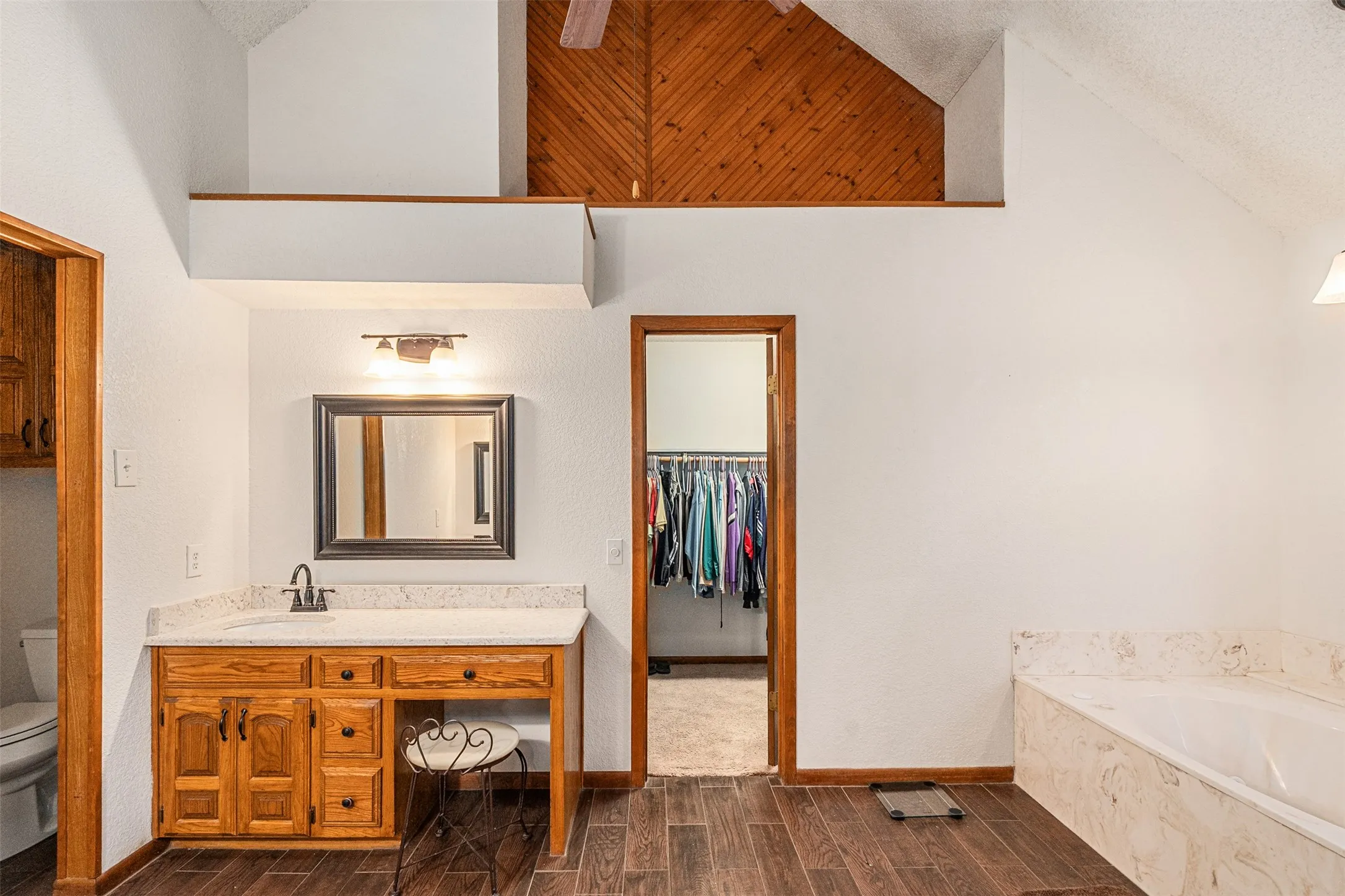 Primary full bath featuring a spacious closet, wood tiled floors, vanity, a textured ceiling, and a garden tub
