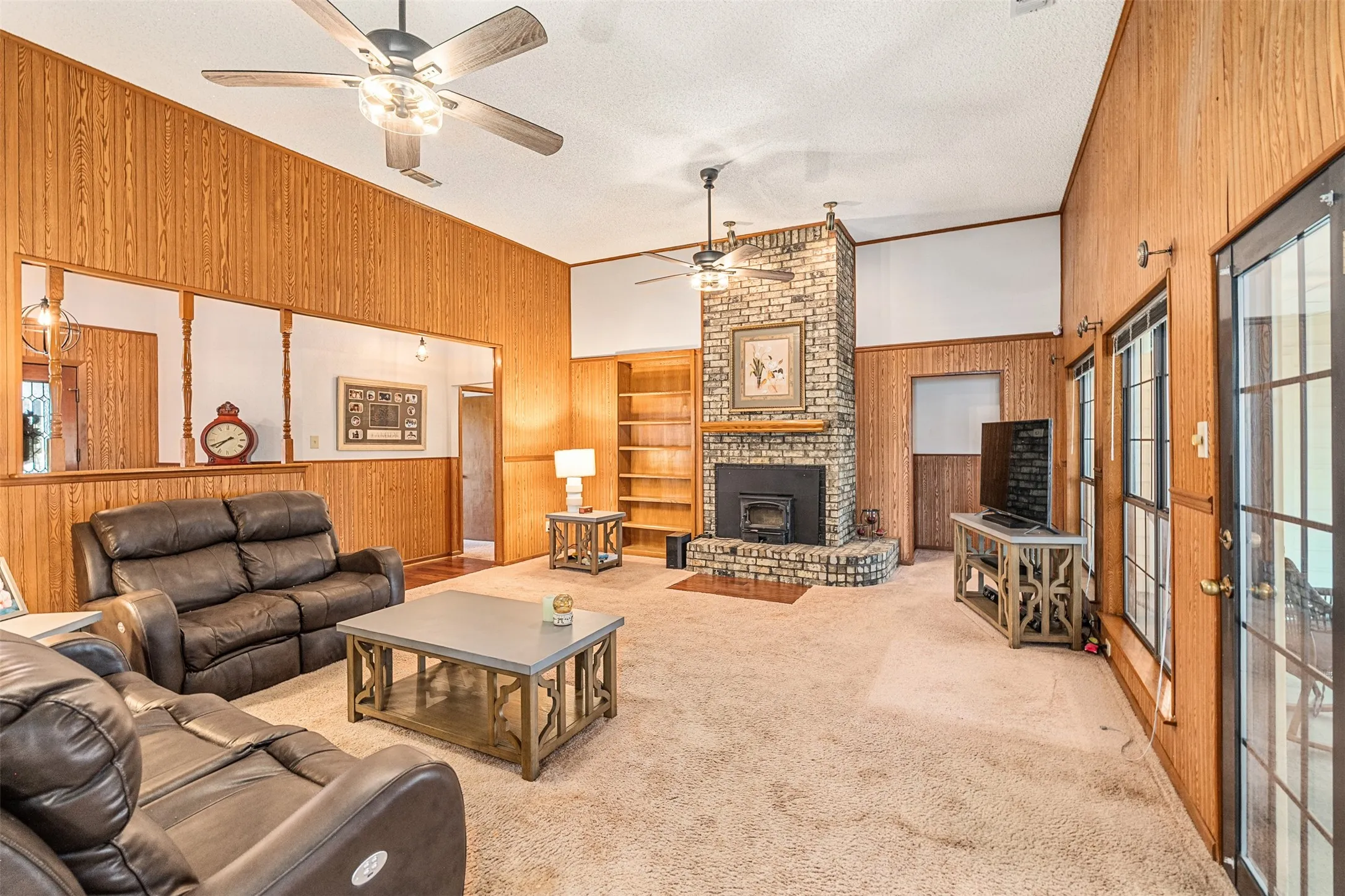 Carpeted living area featuring wood walls, a textured ceiling, built in features, a fireplace, and lofted ceiling