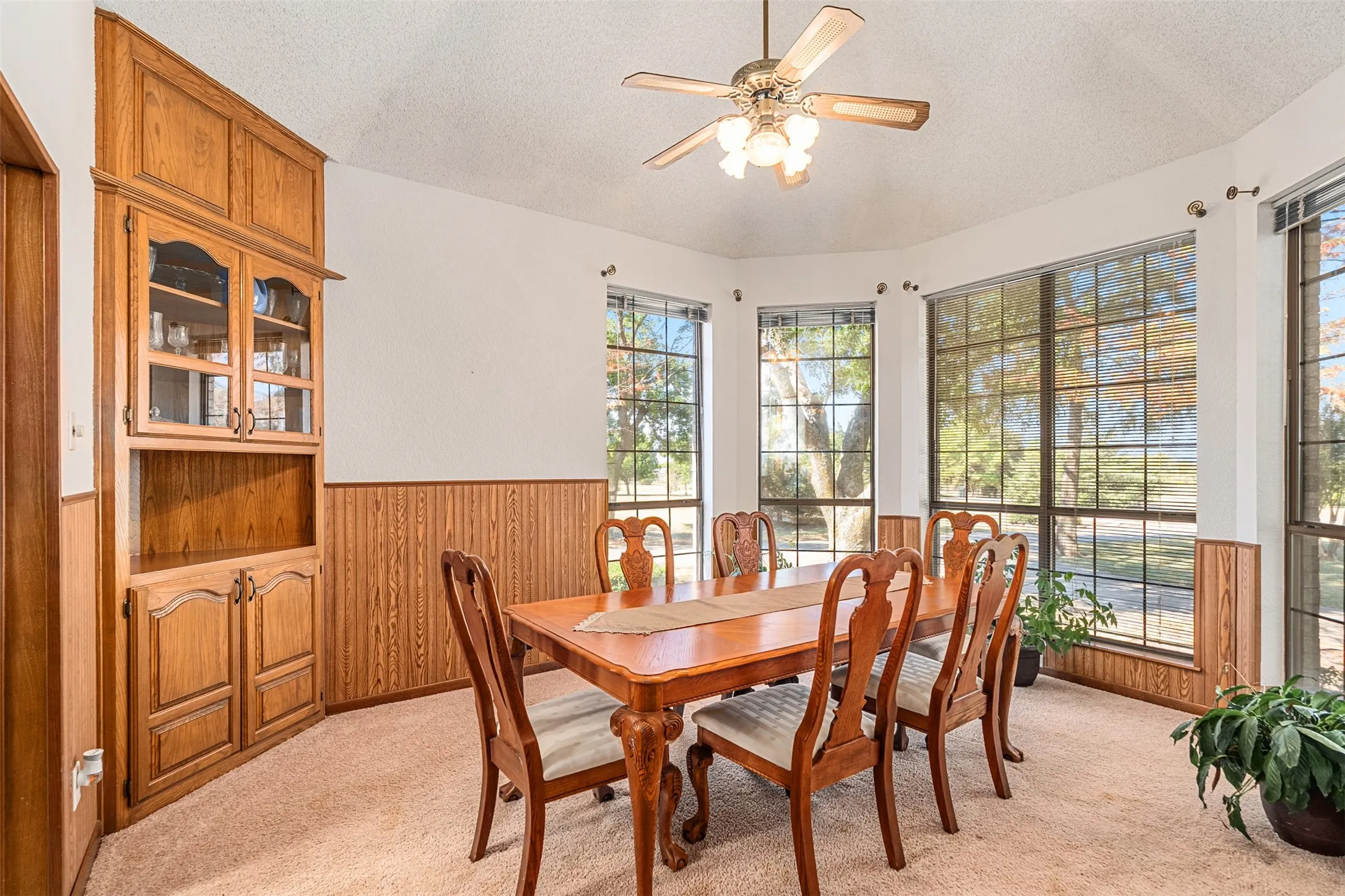 Dining area with wooden walls, a textured ceiling, light carpet, wainscoting, and ceiling fan