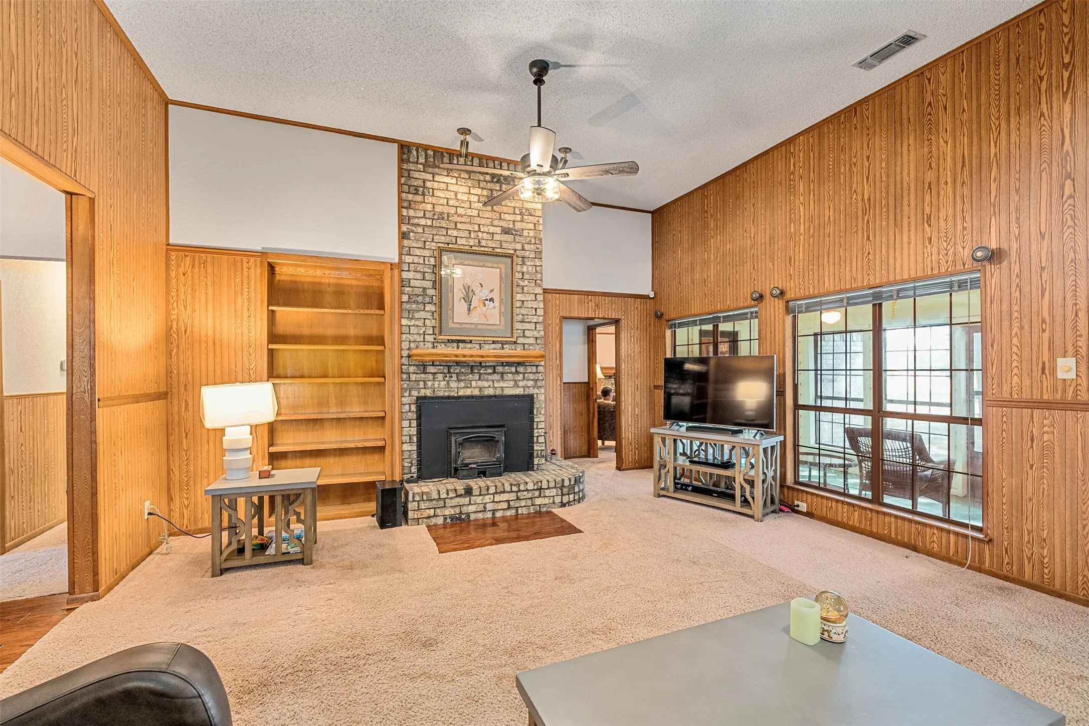 Living area featuring wooden walls, high vaulted ceiling, a textured ceiling, carpet flooring, and ceiling fan