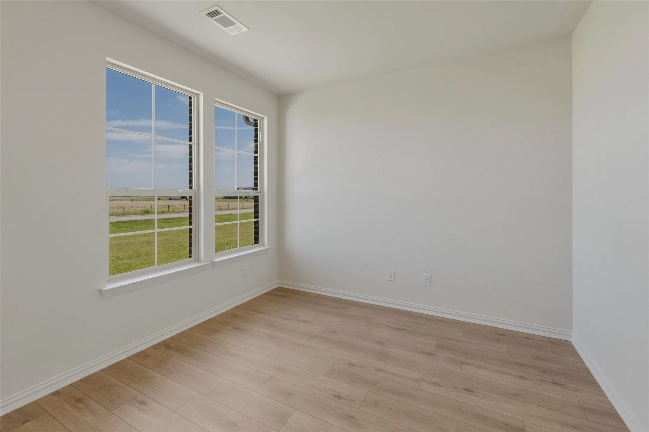 Light-filled interior space featuring two large windows, wood-finish flooring, white baseboards, and a neutral wall color