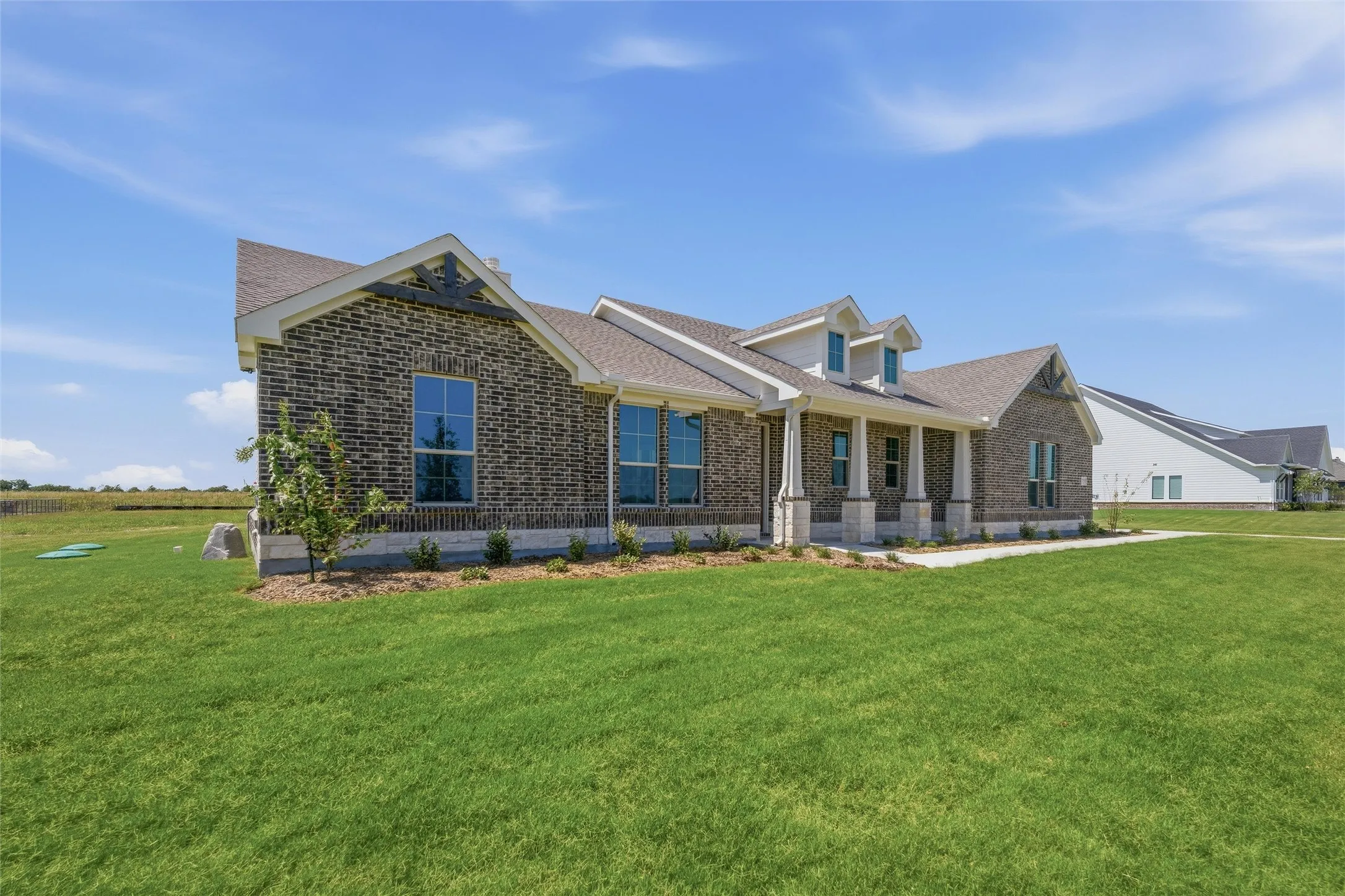 Brick exterior with a gabled roofline, columned front porch, dormer windows, and a manicured lawn
