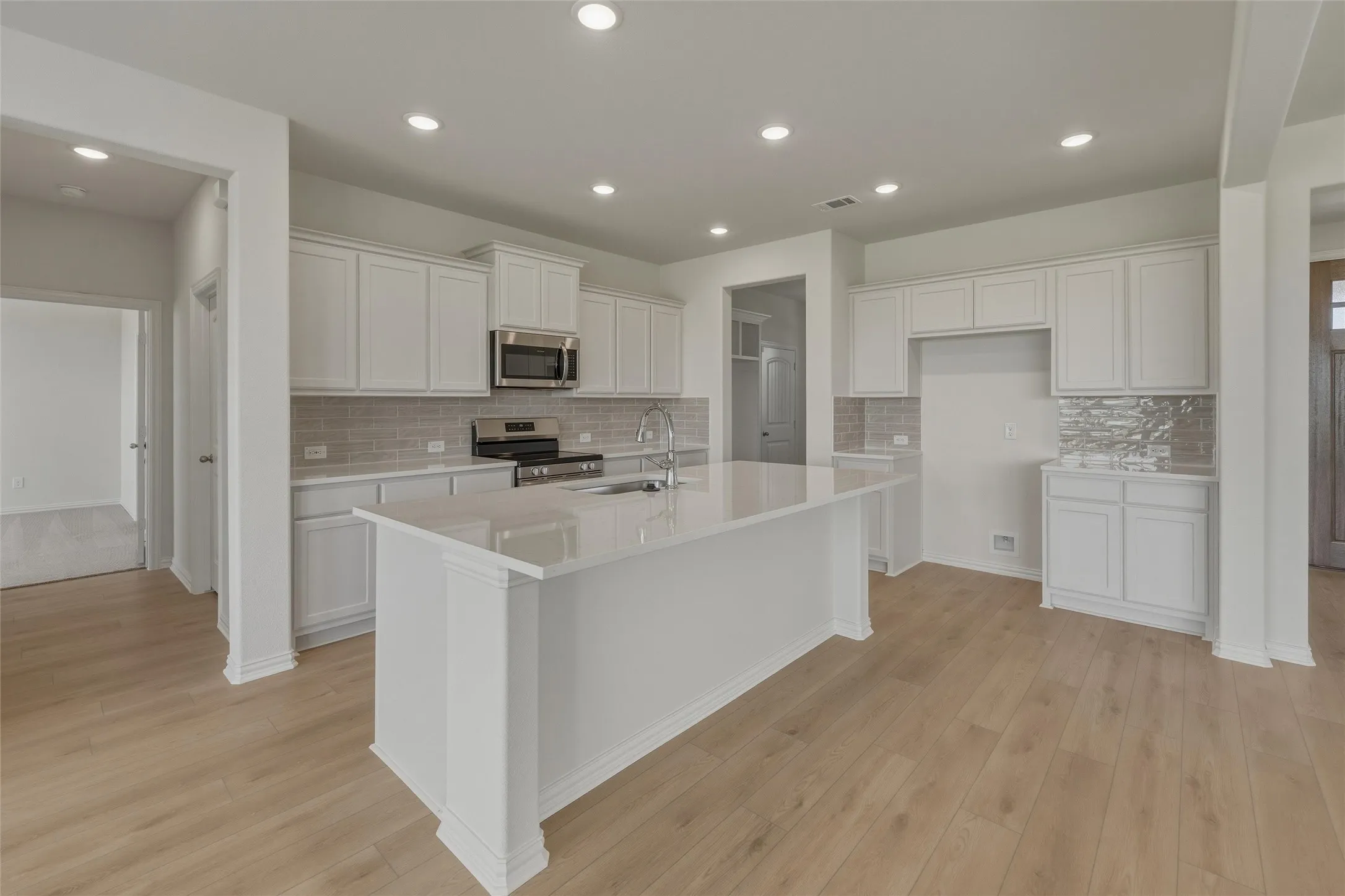 Kitchen featuring a large central island, white cabinetry, stainless steel appliances, tile backsplash, and light wood-finish flooring