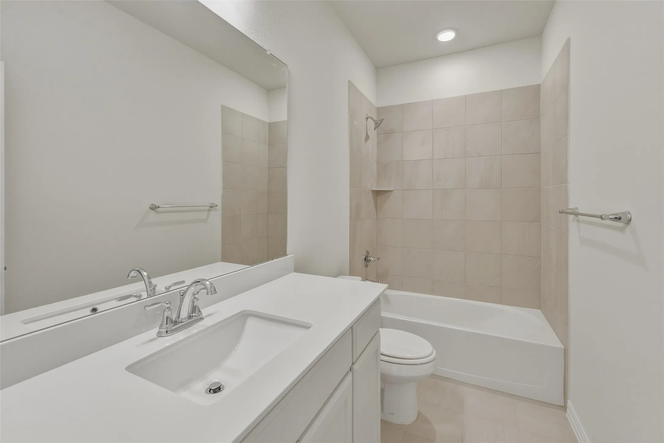 Bathroom featuring a white vanity with an integrated sink, polished chrome faucet, a large frameless mirror, and a tiled shower/tub combination with a built-in shelf