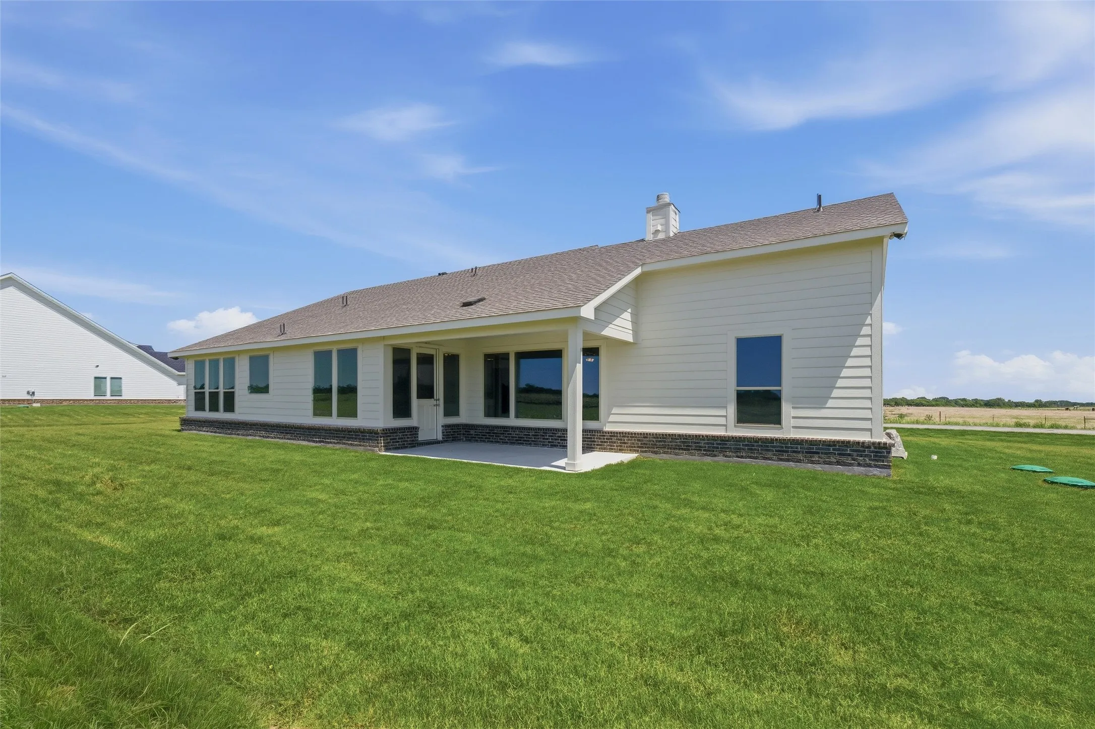 Rear exterior featuring a covered patio, extensive green lawn, white horizontal siding, and a dark stone veneer foundation