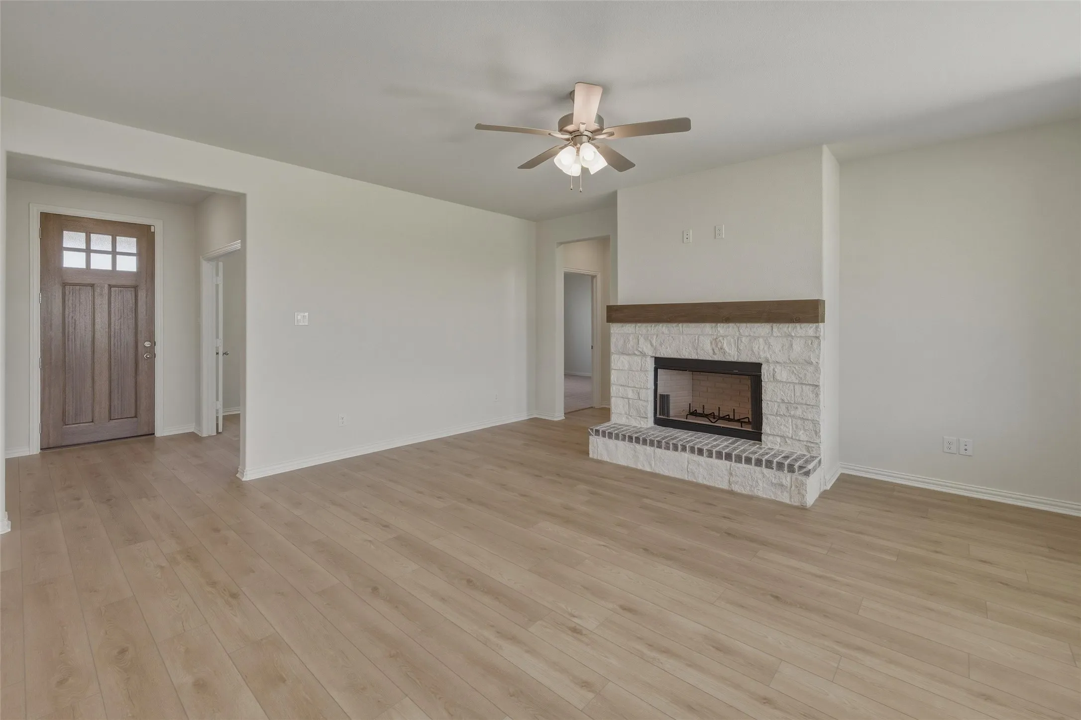 Spacious living area featuring wood-finish flooring, a stone fireplace with a wood mantel, and a ceiling fan with integrated lighting