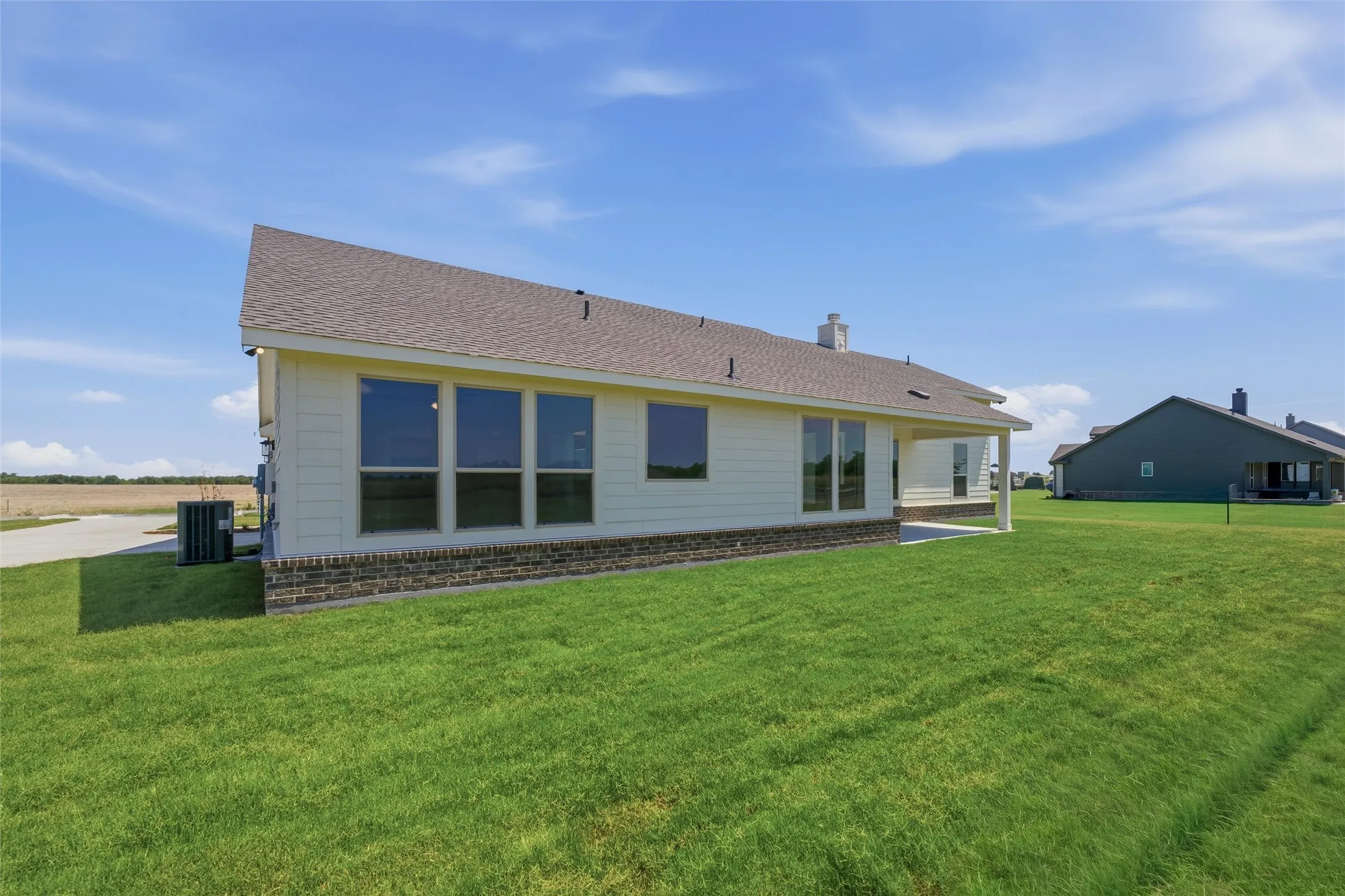 Rear exterior featuring a covered patio, extensive green lawn, and a light-colored siding facade with a dark stone-look skirting
