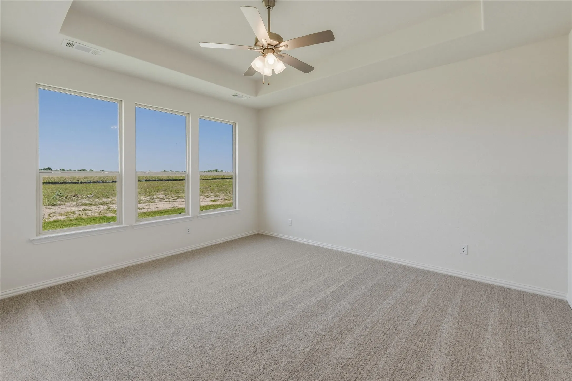 Room featuring a tray ceiling with a mounted ceiling fan, three expansive windows, light-toned carpeting, and neutral wall paint