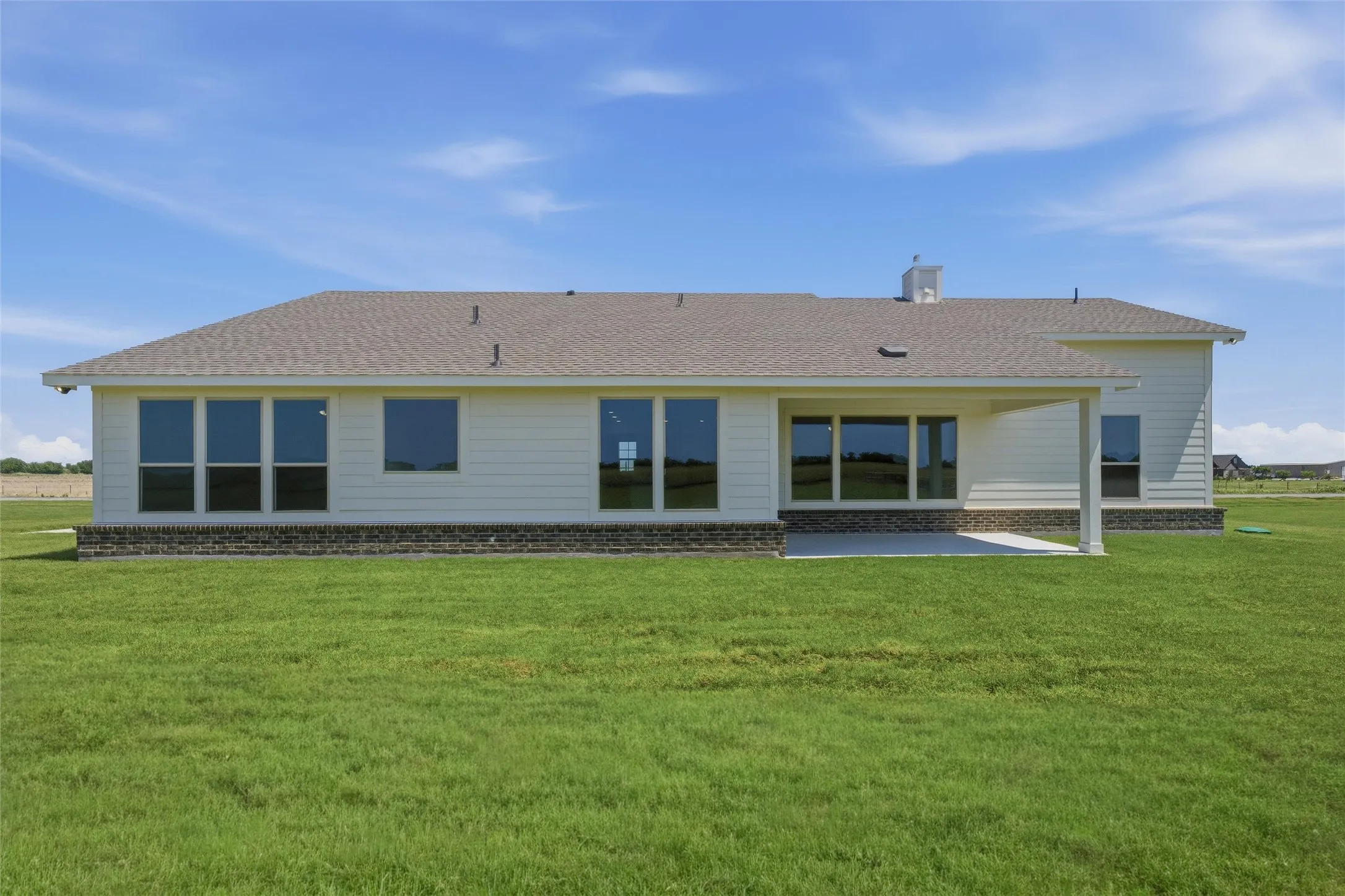 Expansive rear exterior featuring a covered patio, multiple large windows, a light-colored siding facade, and a stone-style foundation