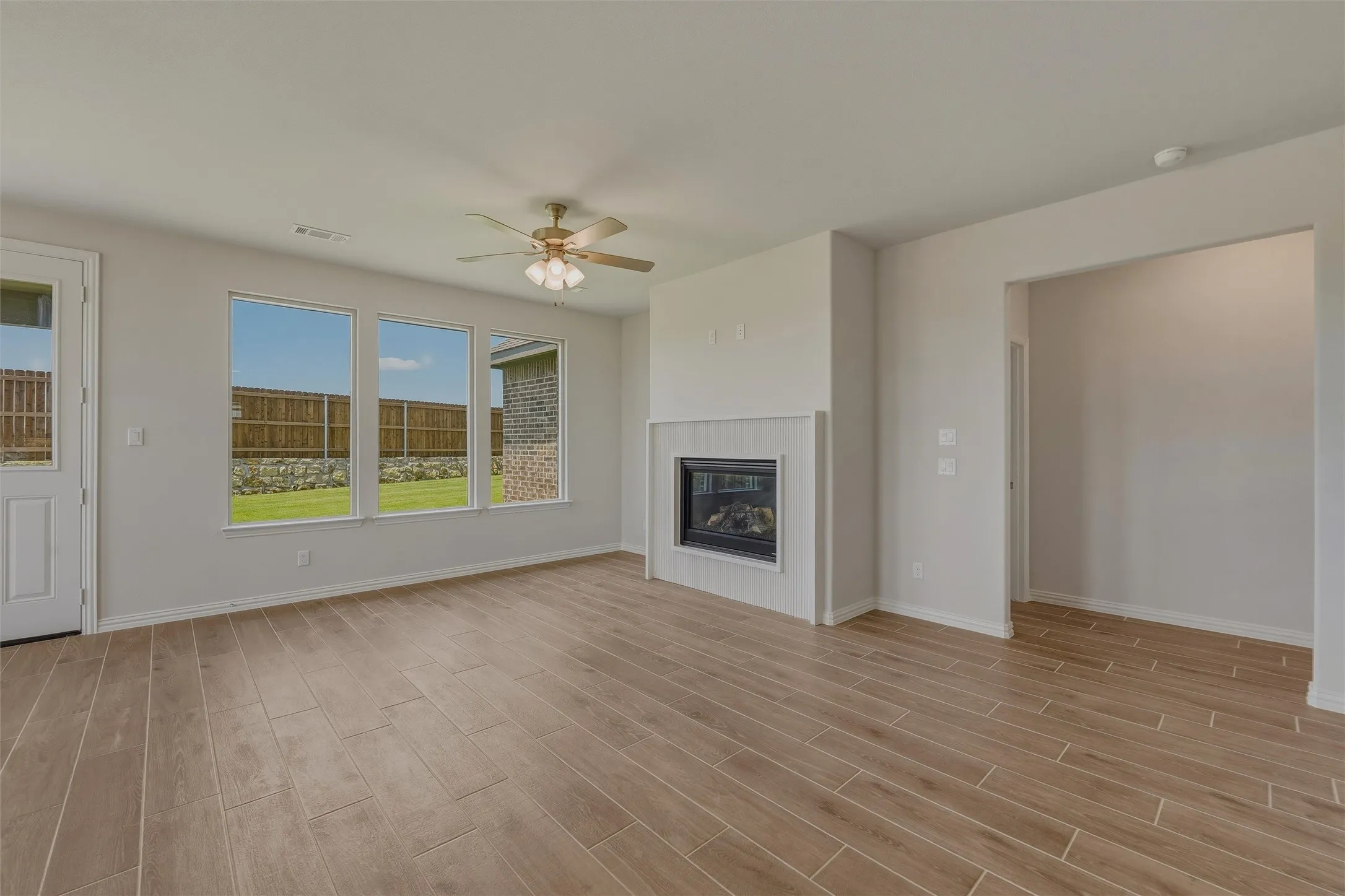 Spacious living area featuring wood-finish plank flooring, a contemporary fireplace, and a ceiling fan