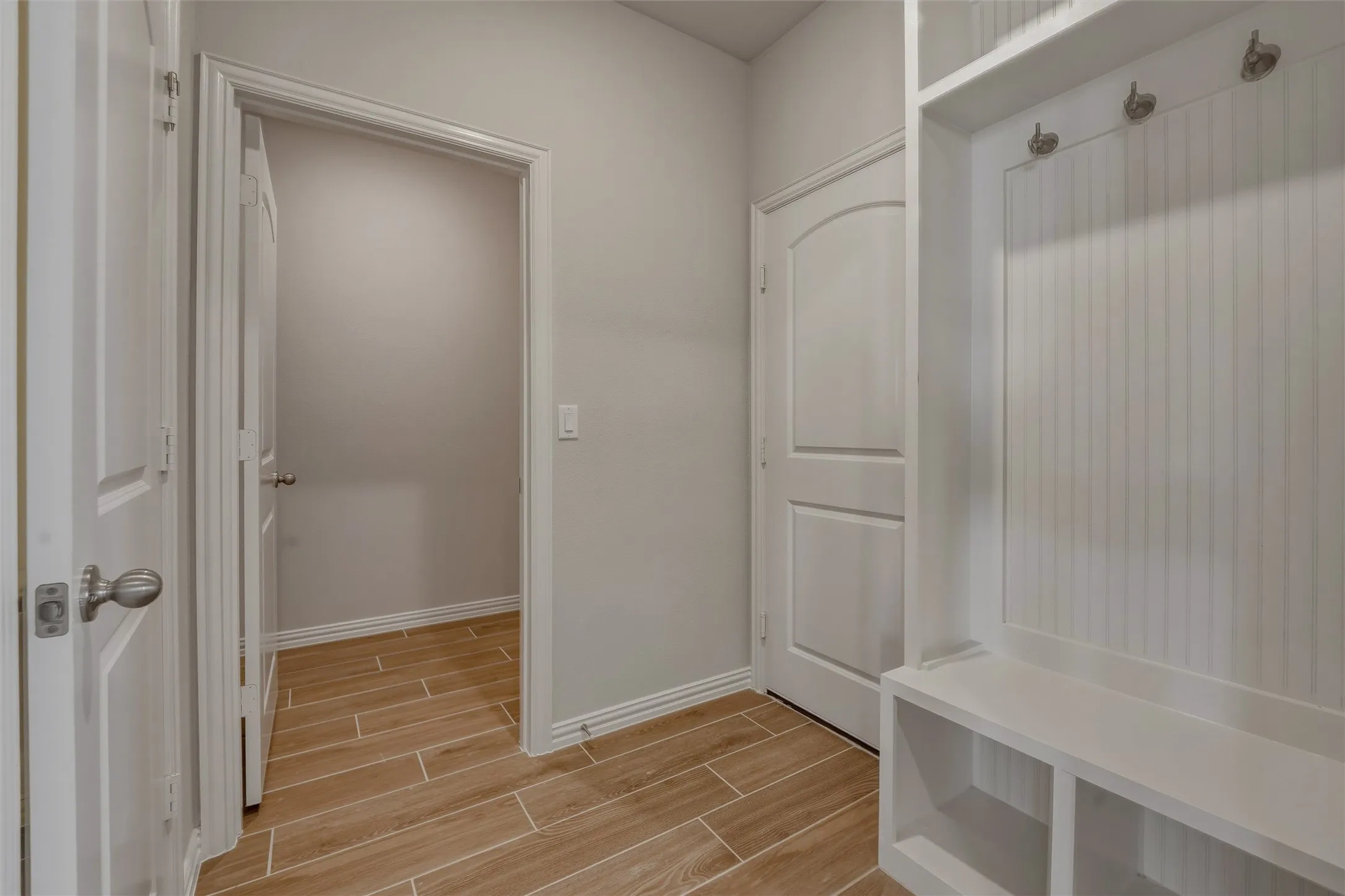 Mudroom featuring built-in storage with hooks and cubbies, wood-finish flooring, two paneled doors, and light gray wall paint