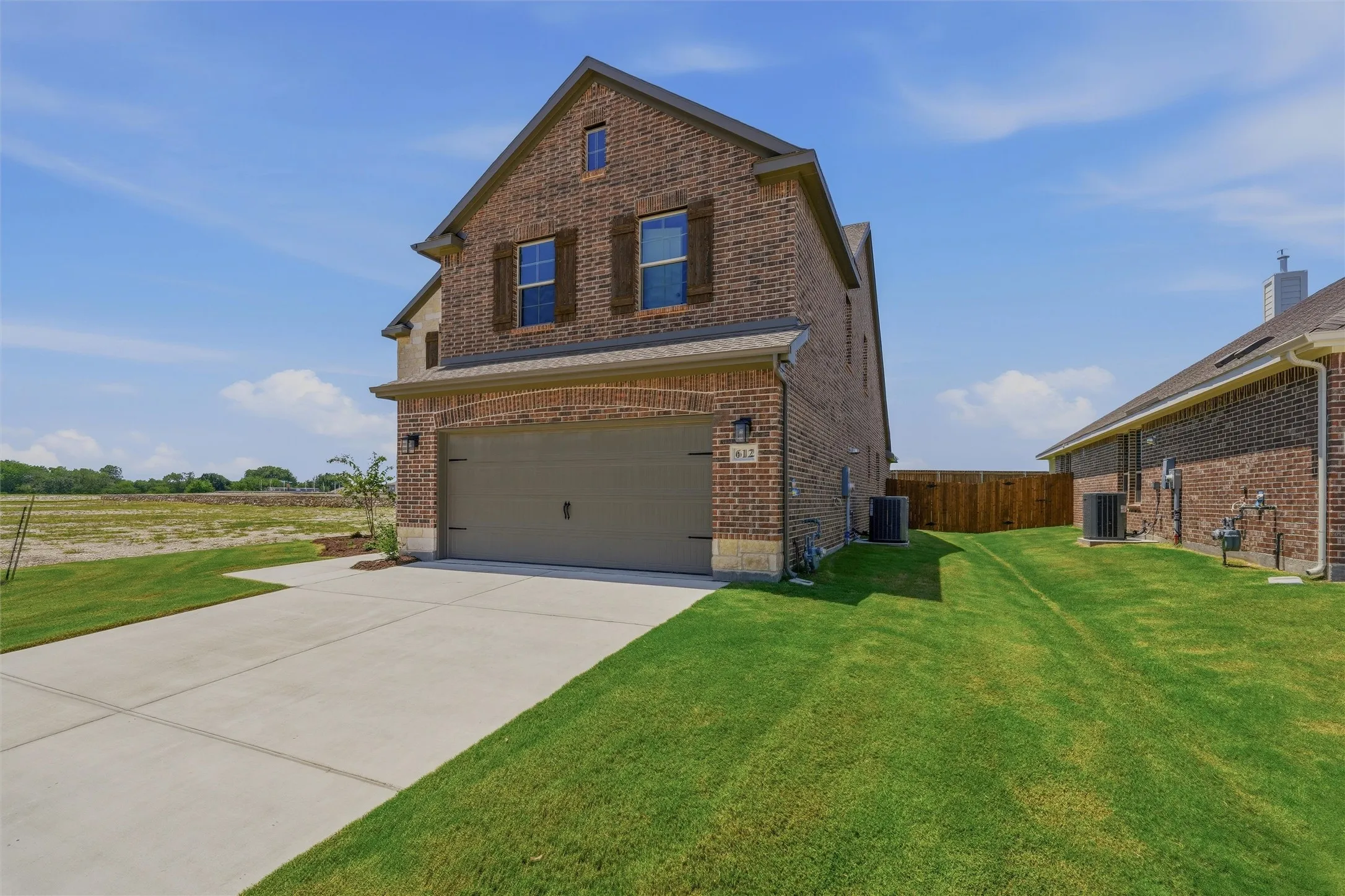 Two-story brick exterior with stone accents, featuring a two-car garage with an arched brick header, wood-tone shutters, and a concrete driveway