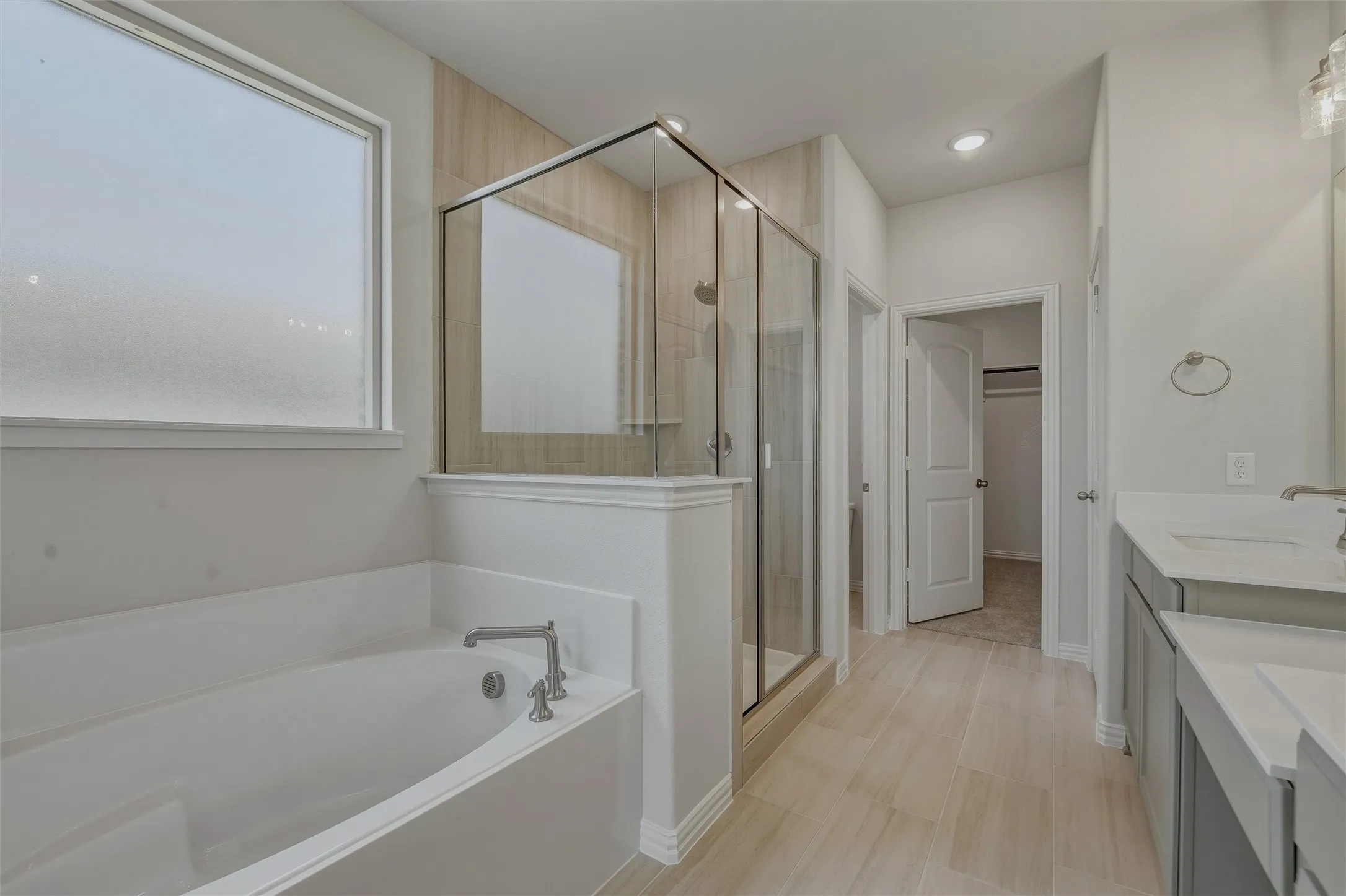 Spacious bathroom featuring a built-in tub with chrome fixtures, a clear glass shower enclosure with tiled walls, dual vanity sinks with light-colored countertops, and wood-finish tile flooring