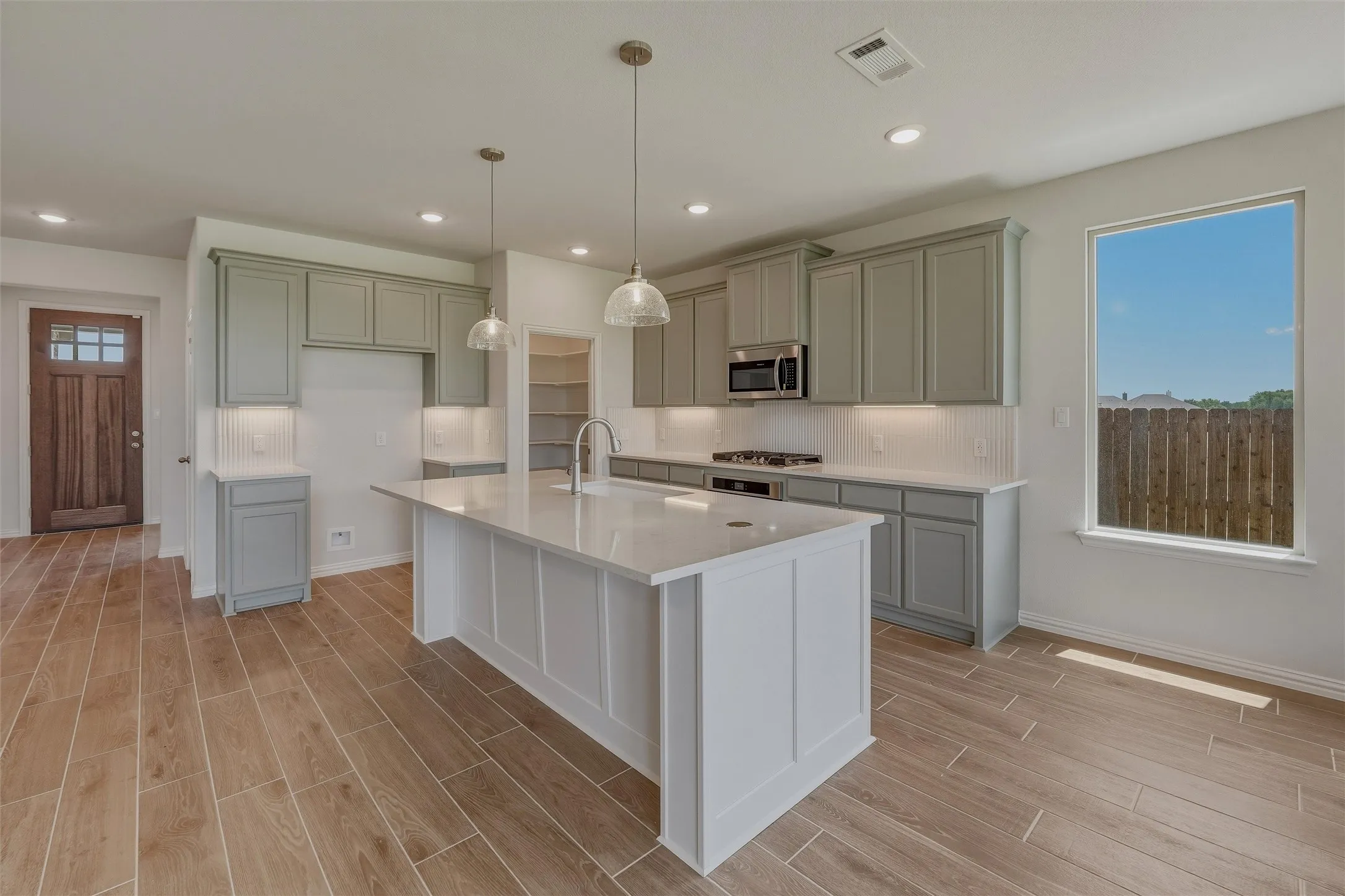 Modern kitchen featuring a large central island with a sink, pendant lighting, and light-toned countertops