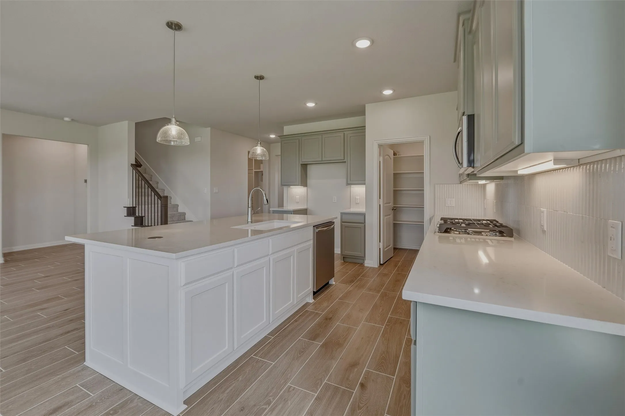 Modern kitchen featuring a large island with white panel cabinetry, light-toned countertops, and two suspended glass pendant lights