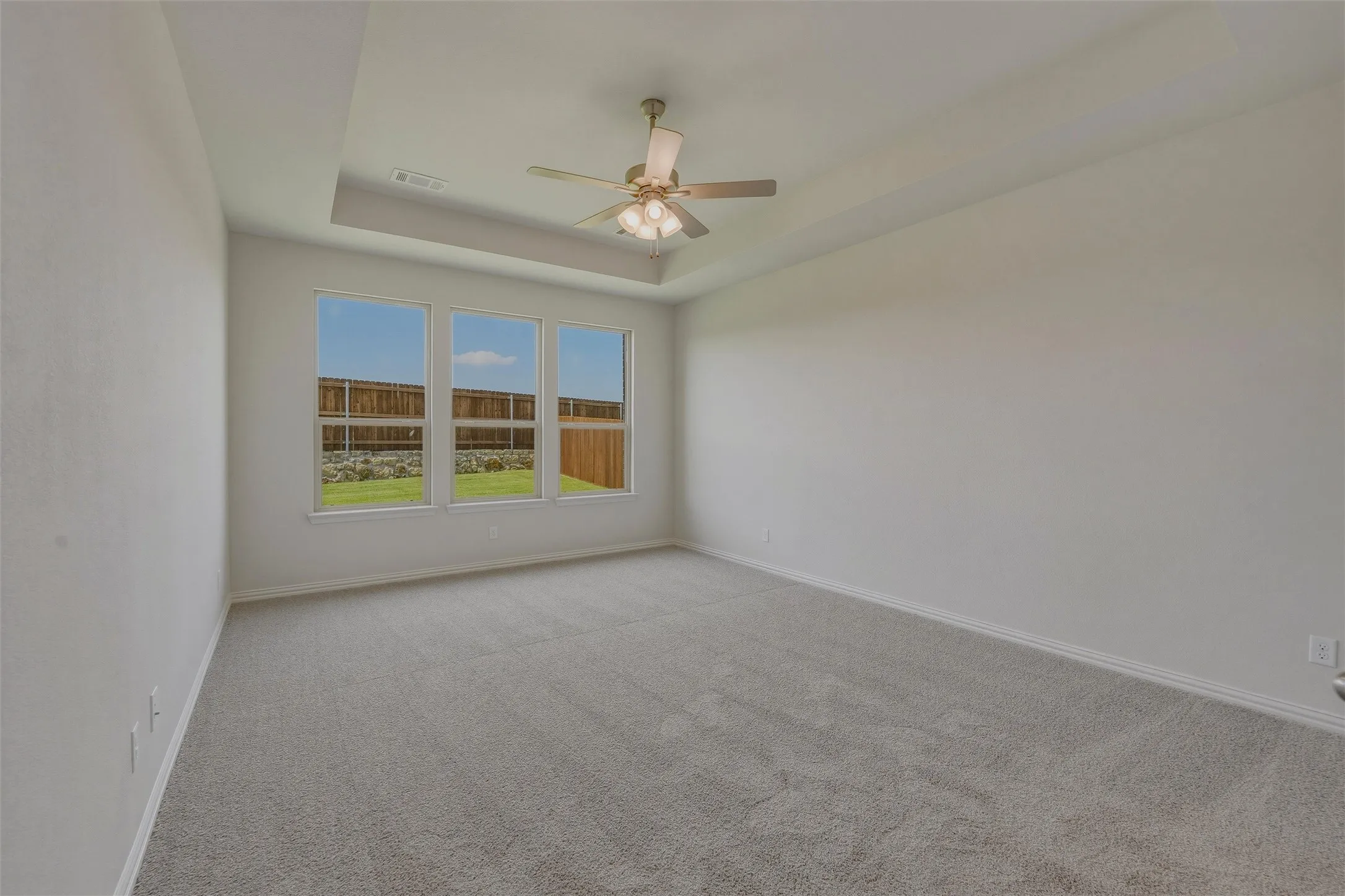Carpeted room featuring a tray ceiling with a ceiling fan