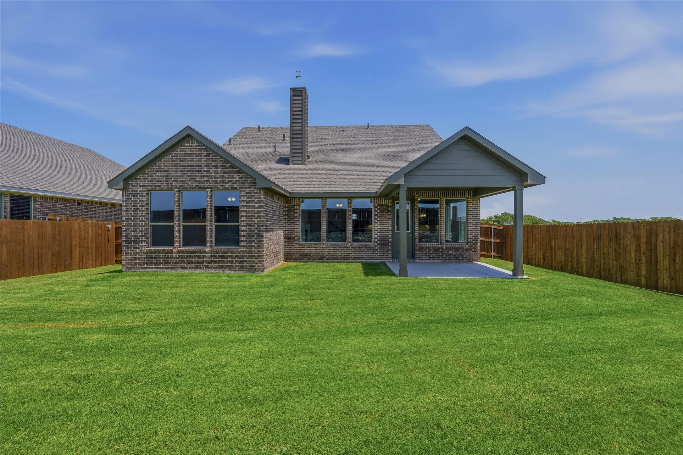 Spacious backyard featuring a covered patio, extensive green lawn, and a privacy fence