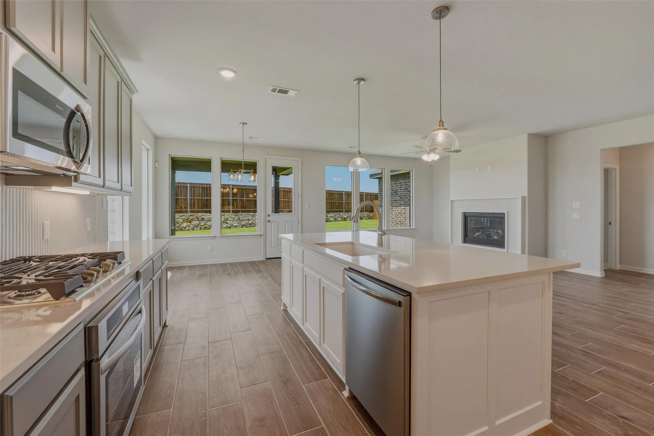 Contemporary kitchen featuring a large island with an undermount sink and stainless steel dishwasher, light-toned countertops, and wood-finish tile flooring