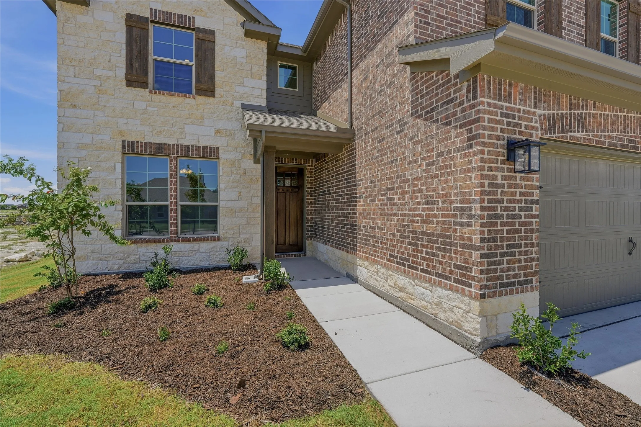 Exterior featuring stone and brick masonry, a wood-finish entry door with glass inserts, wood-finish window shutters, and an attached garage with a carriage-style door