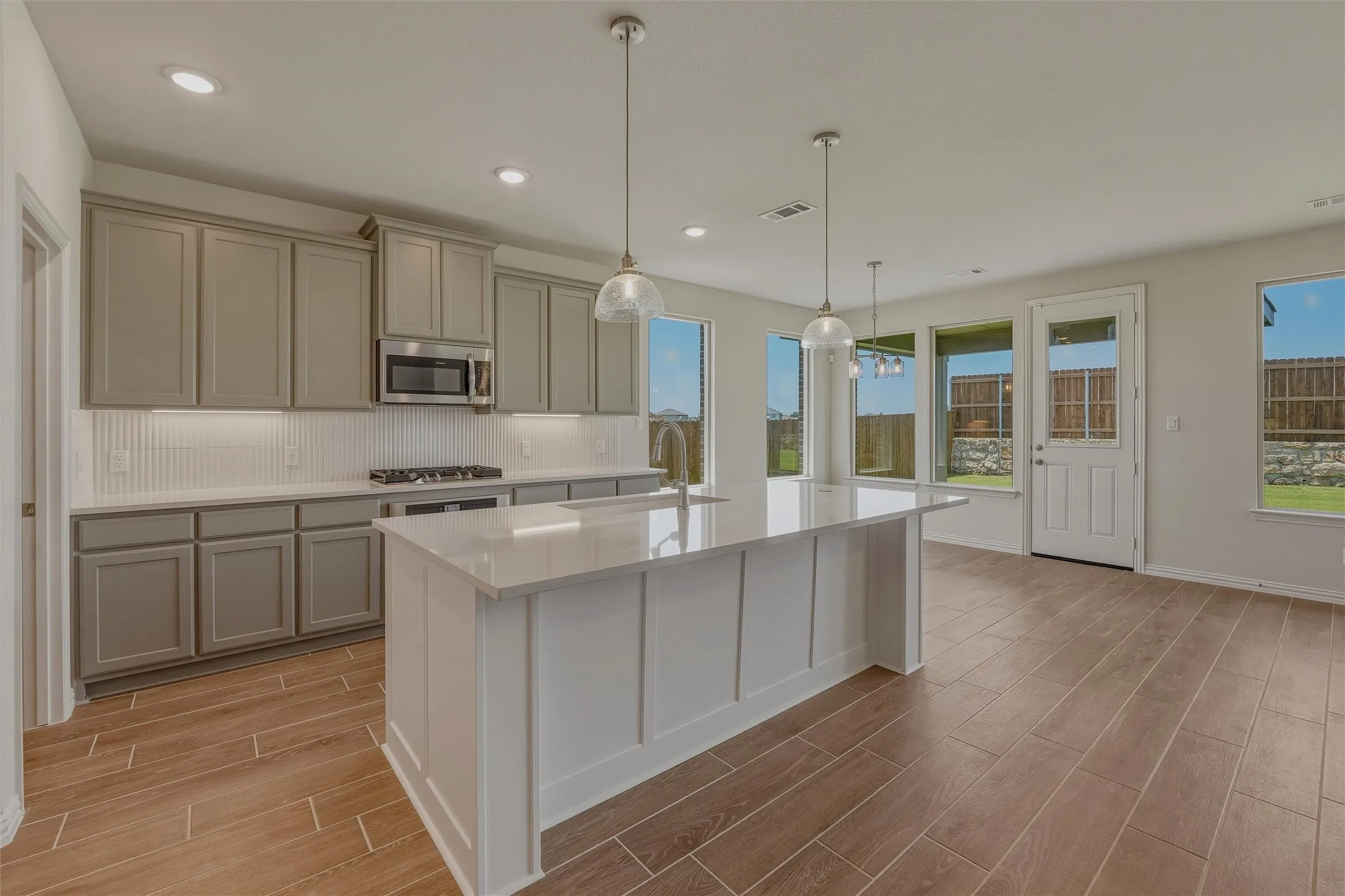 Open-concept kitchen featuring an island with a light-toned countertop, gray cabinetry, stainless steel appliances, and wood-finish flooring