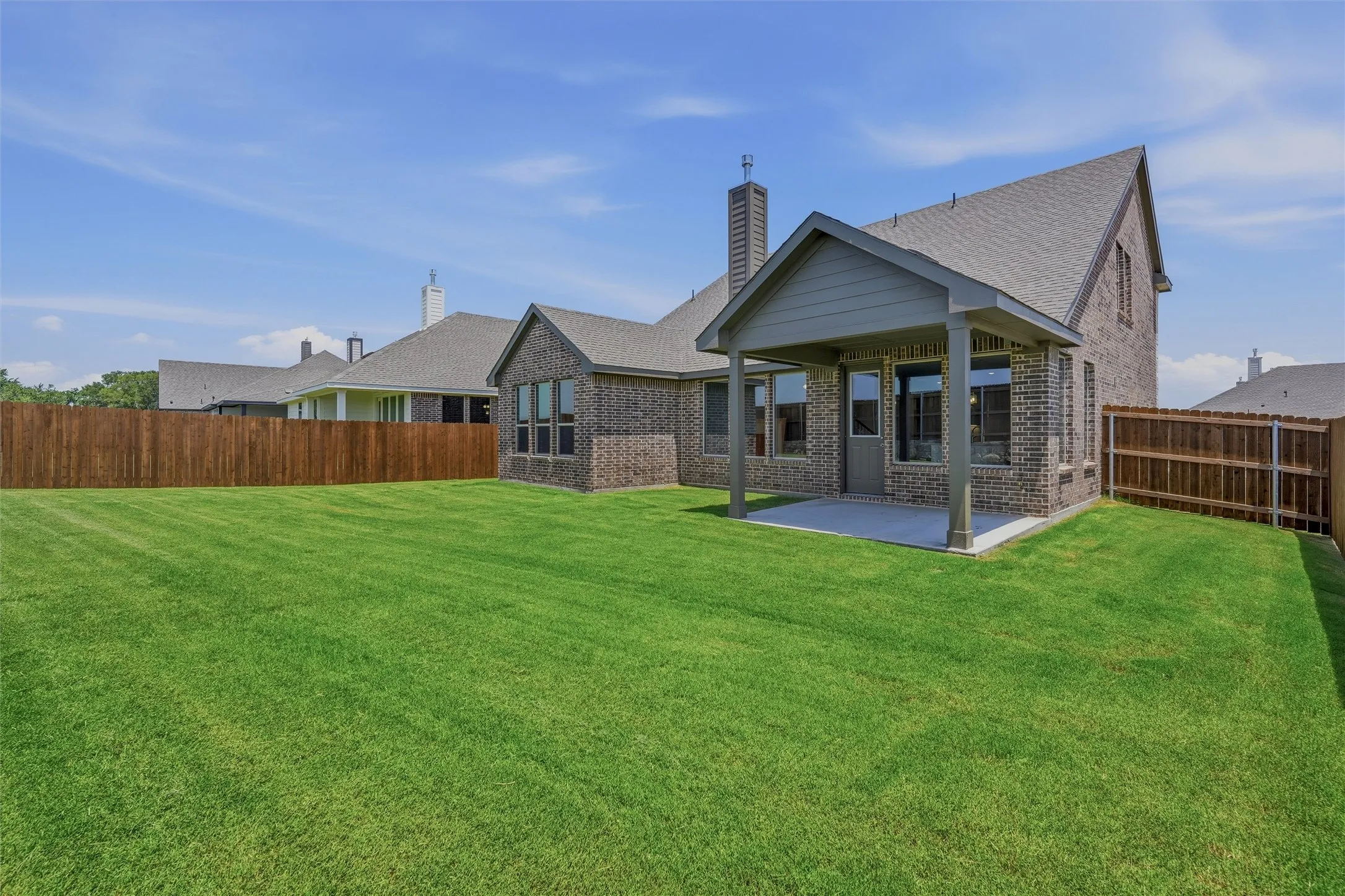 Expansive rear yard featuring a covered patio, dark brick exterior, multiple windows, and a wood privacy fence