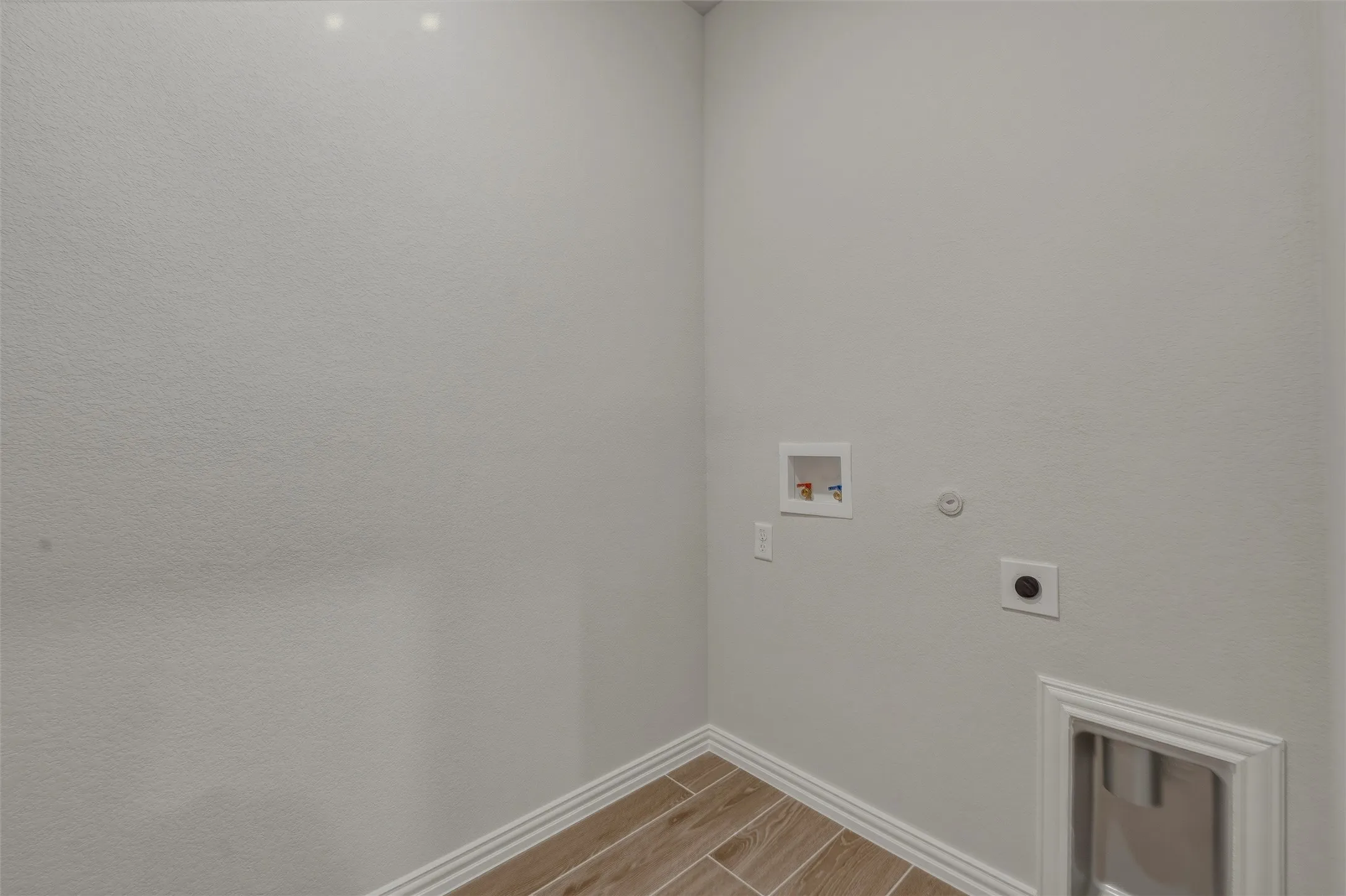 Laundry area featuring wood-finish tile flooring, light-toned wall paint, and white baseboards