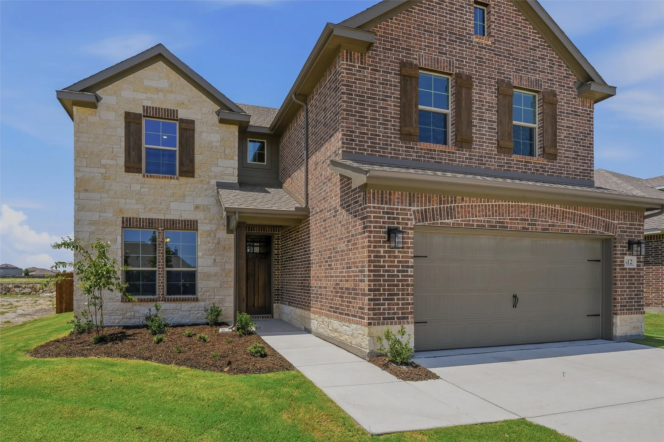 Two-story facade featuring a stone and brick exterior, a two-car garage with an arched brick detail, prominent windows with dark shutters, and a covered entry
