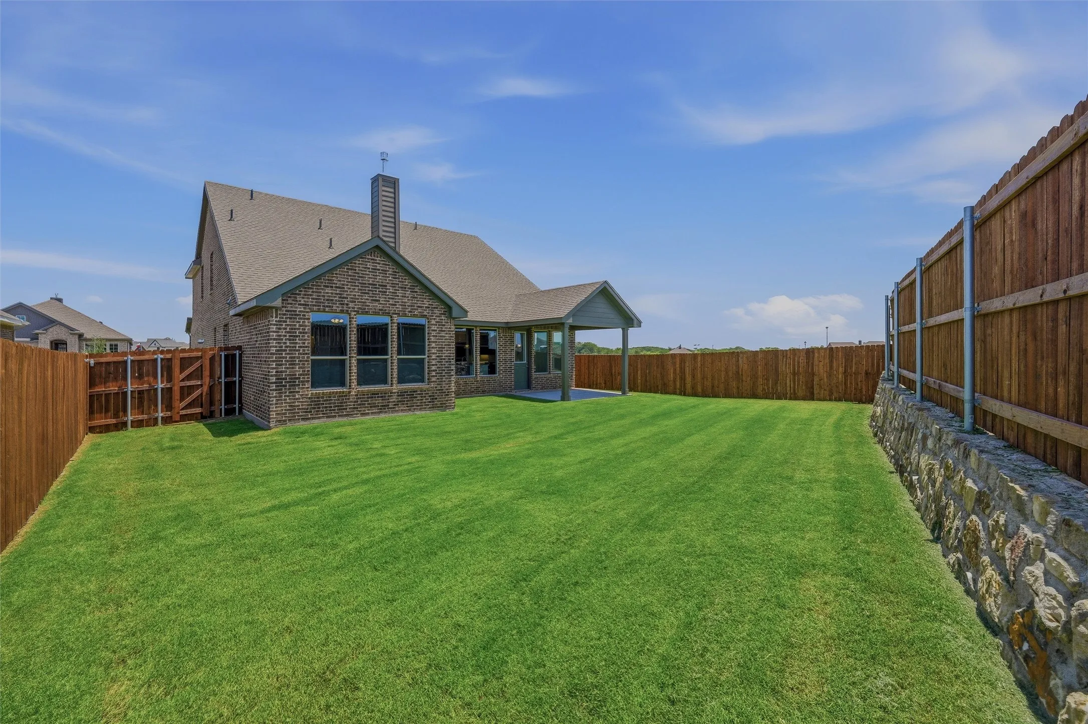 Expansive green lawn with a covered patio, full privacy fencing, and stone retaining wall