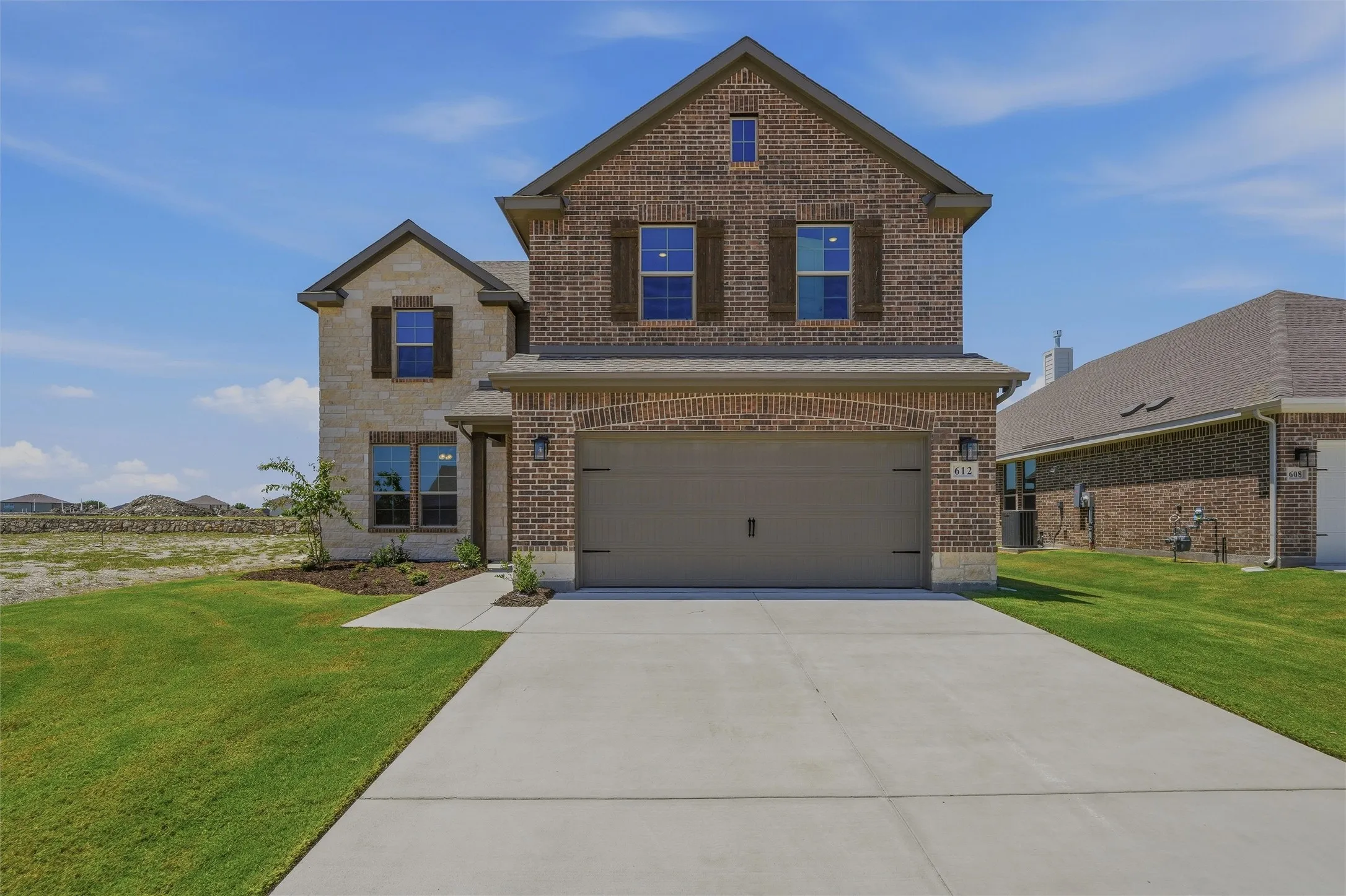 Brick and stone exterior featuring a two-car garage with an arched entry, a concrete driveway, and a front walkway
