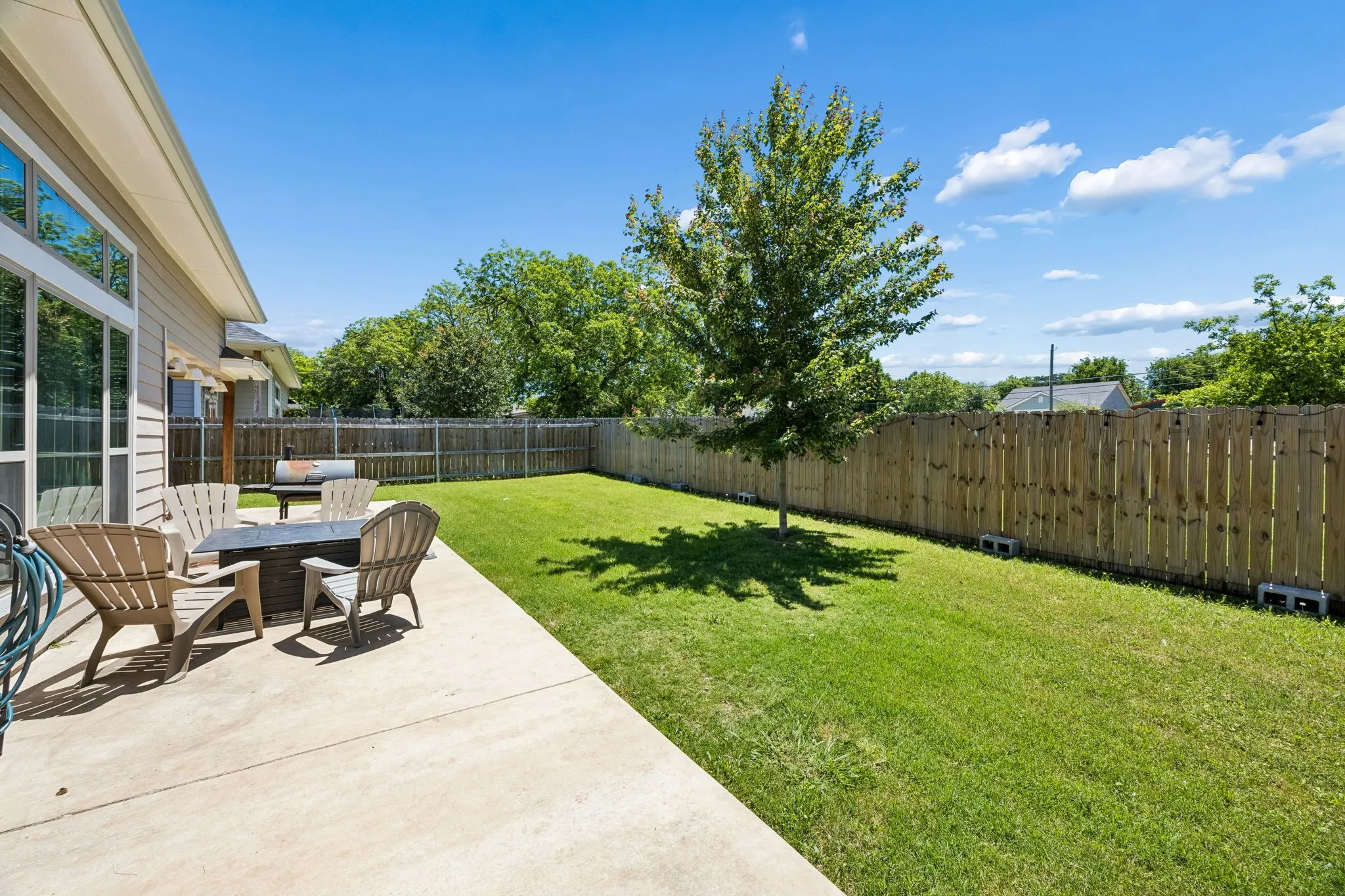 Expansive backyard featuring a concrete patio, mature tree, and full privacy fencing