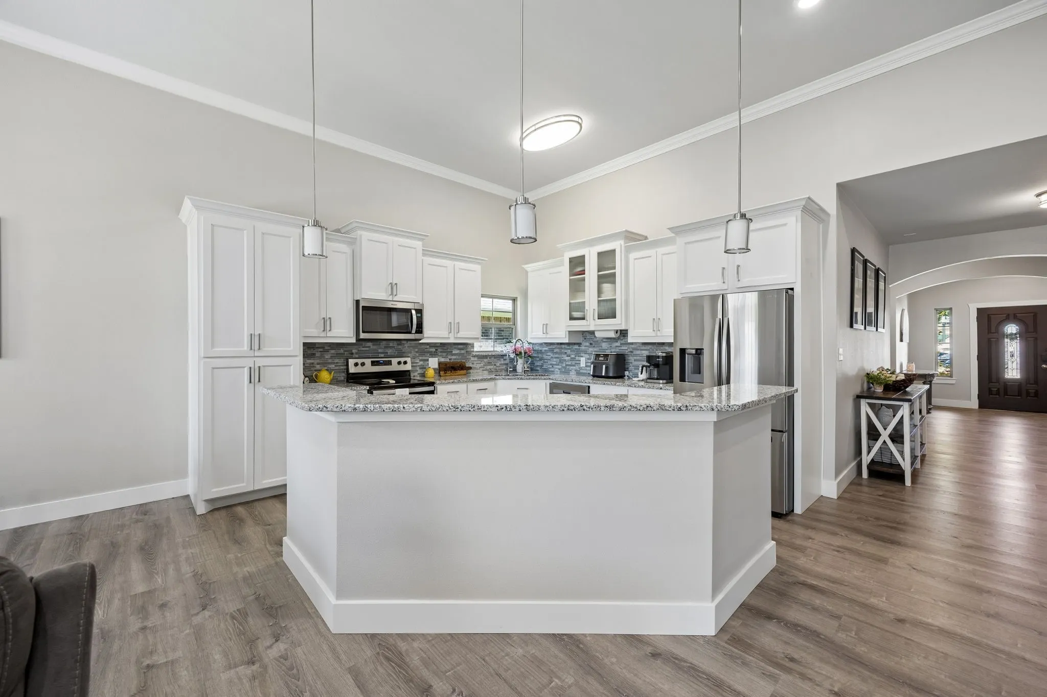 Kitchen featuring white cabinetry, stainless steel appliances, a multi-tone tile backsplash, light-toned countertops, and wood-finish flooring