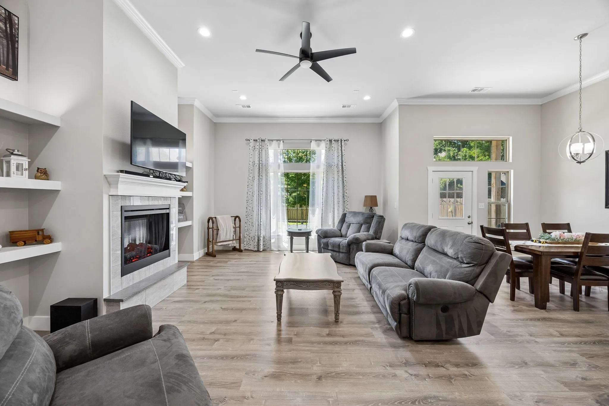 Open-concept living space featuring wood-finish flooring, a tiled fireplace with a white mantel, recessed lighting, and a ceiling fan