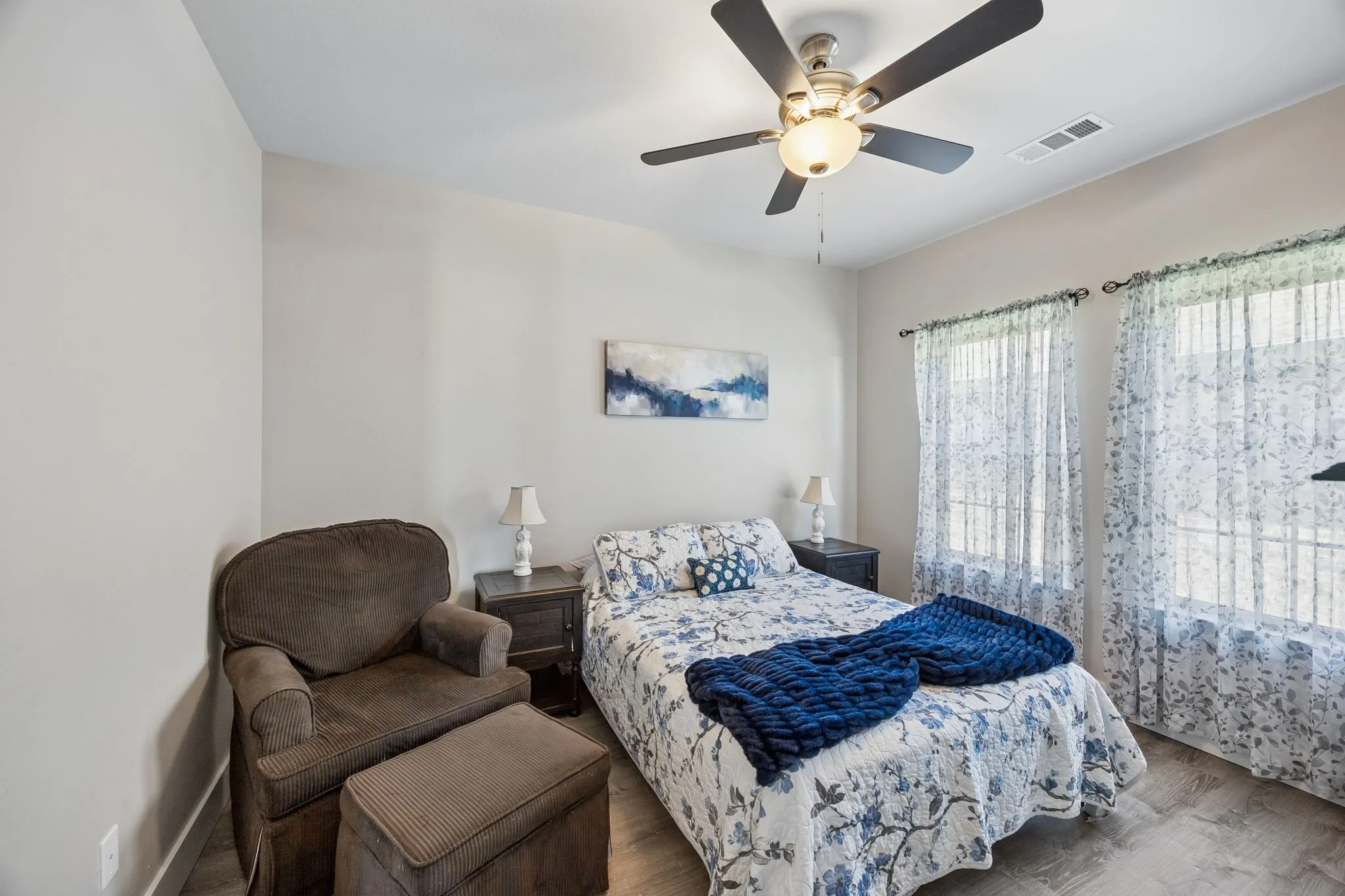 Bright room featuring wood-finish flooring, a ceiling fan with integrated lighting, and dual windows