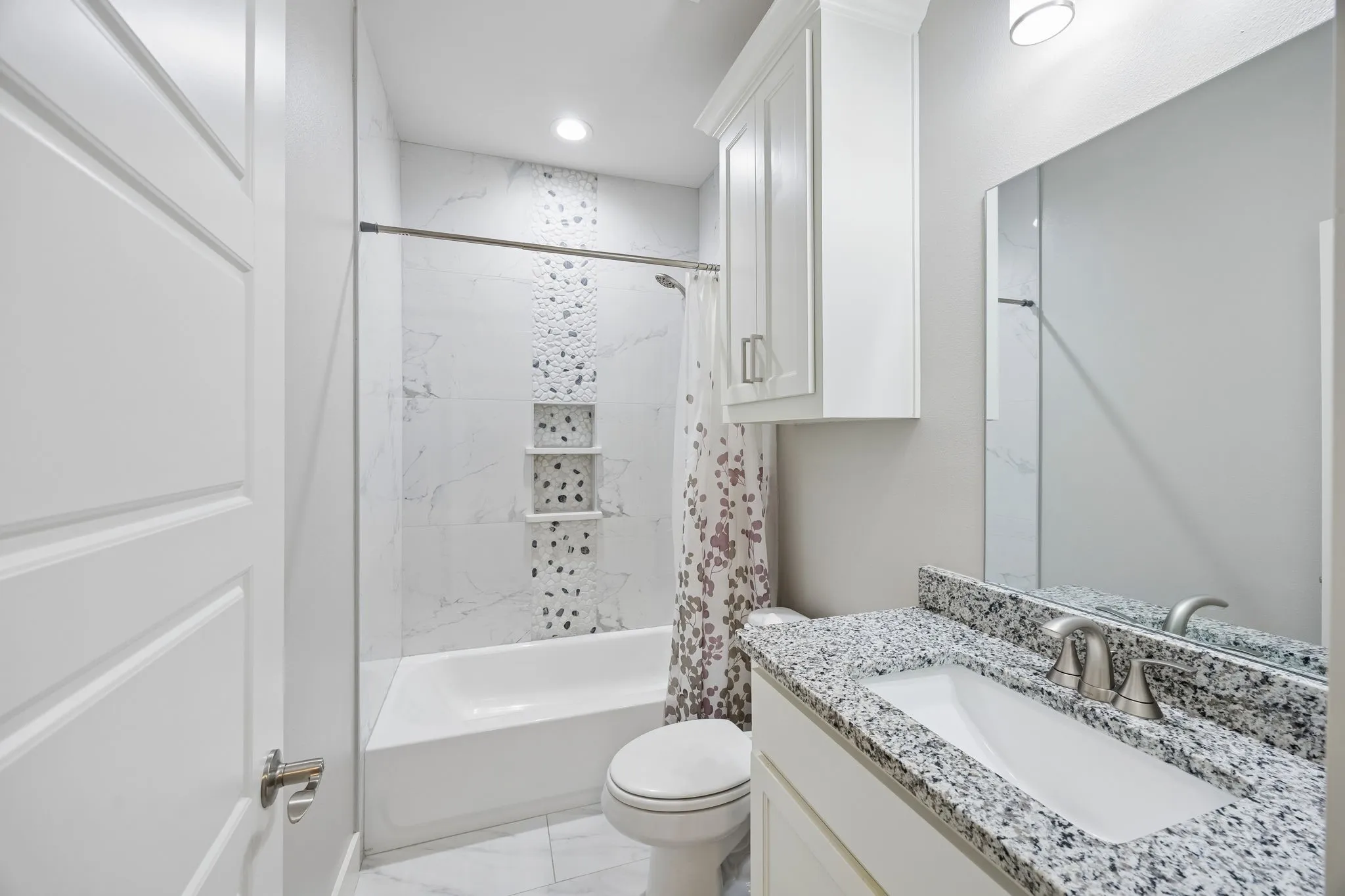 Full bathroom with a white tub and shower combination, featuring a tiled surround with a decorative pebble-style accent