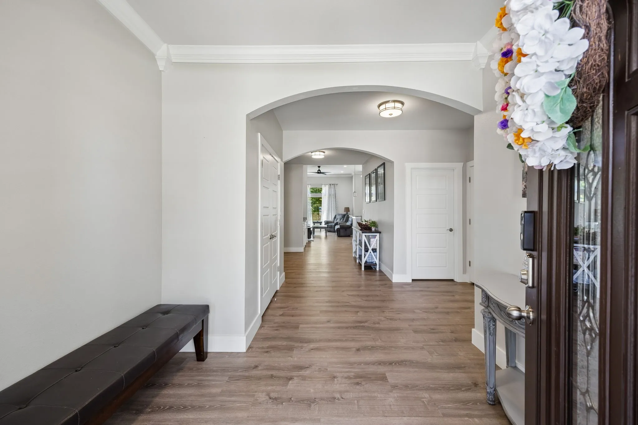 Entryway featuring wood-finish flooring, light gray wall paint, white crown molding, and an arched doorway