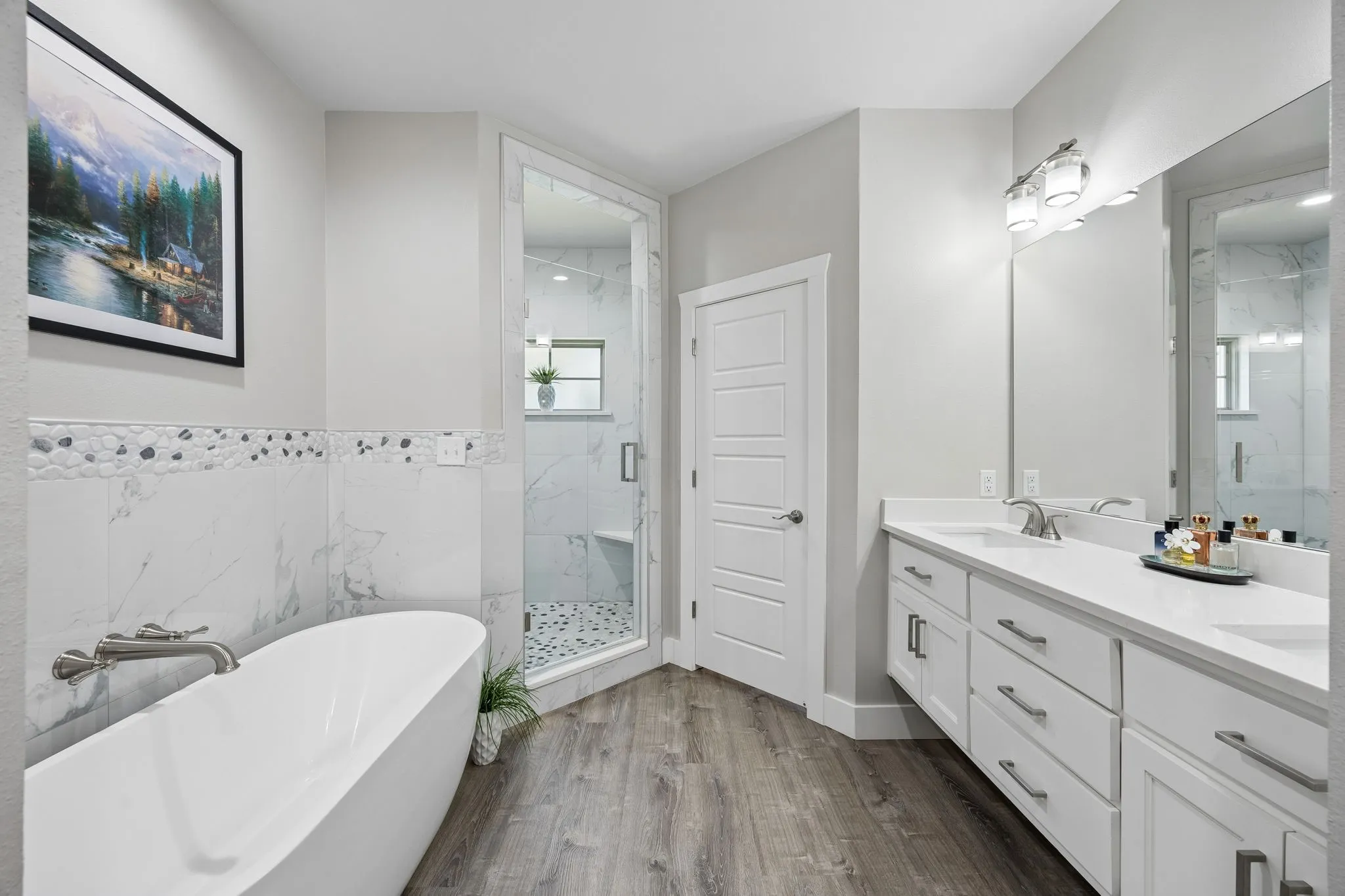 Bathroom featuring a freestanding soaking tub with brushed nickel fixtures, a large walk-in shower with glass enclosure and mosaic tile floor, a double vanity with stone countertops, and wood-finish flooring