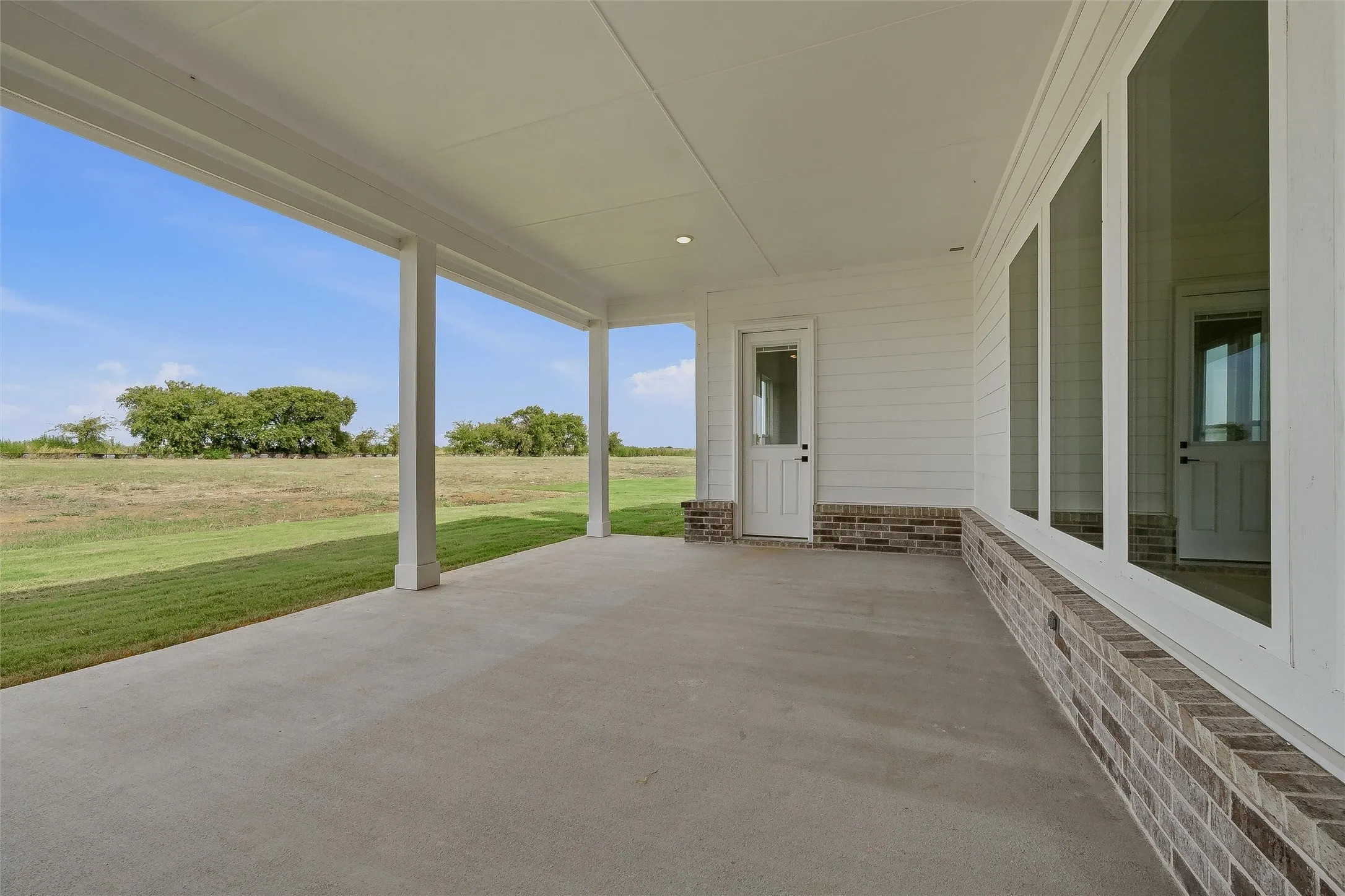Expansive covered patio with concrete flooring, recessed lighting, and brick wainscoting