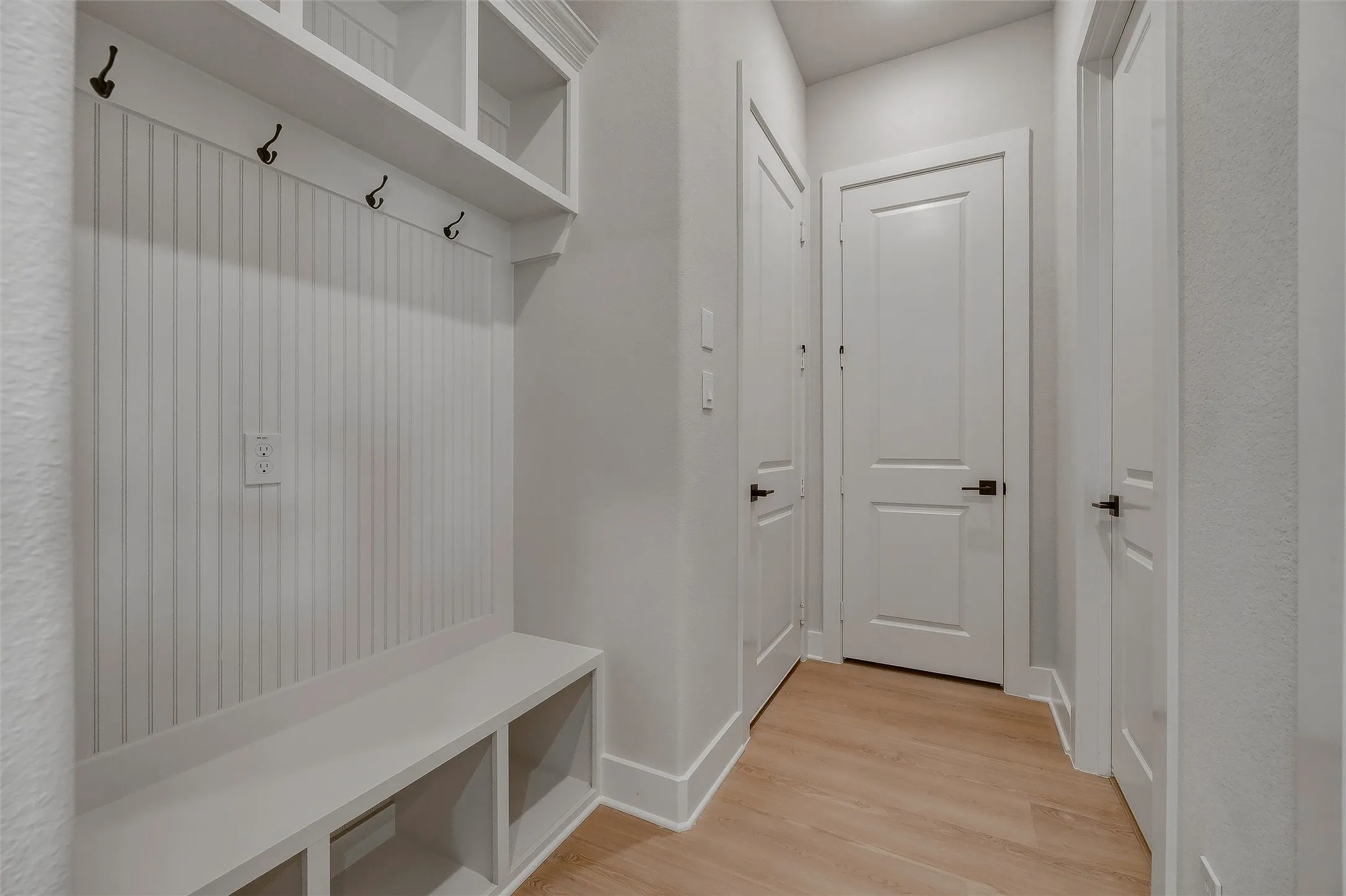 Entryway featuring beadboard accent wall, built-in bench with storage cubbies, integrated shelving, and wood-finish flooring