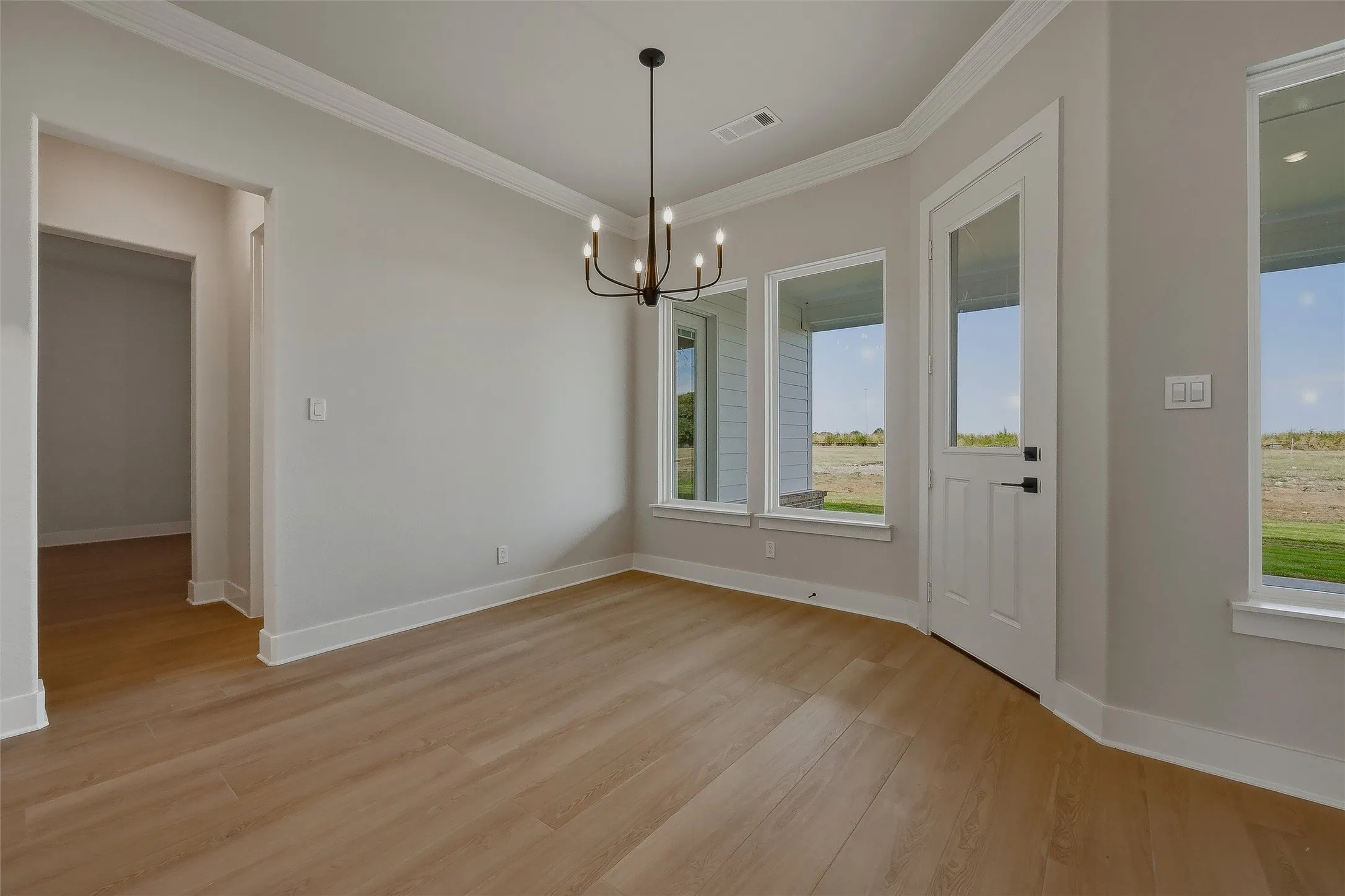 Wood-finish flooring, abundant natural light, a modern black chandelier, crown molding, and a white paneled door with glass insert