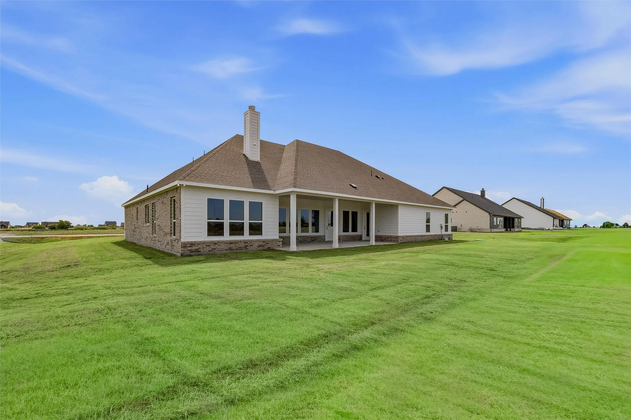 Expansive rear yard with a covered patio, multiple large windows, and a brick and siding exterior