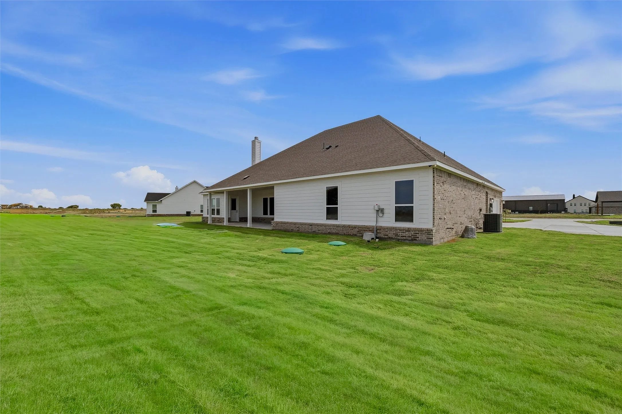 Expansive green lawn surrounds the residence, featuring brick and siding exterior and a covered patio