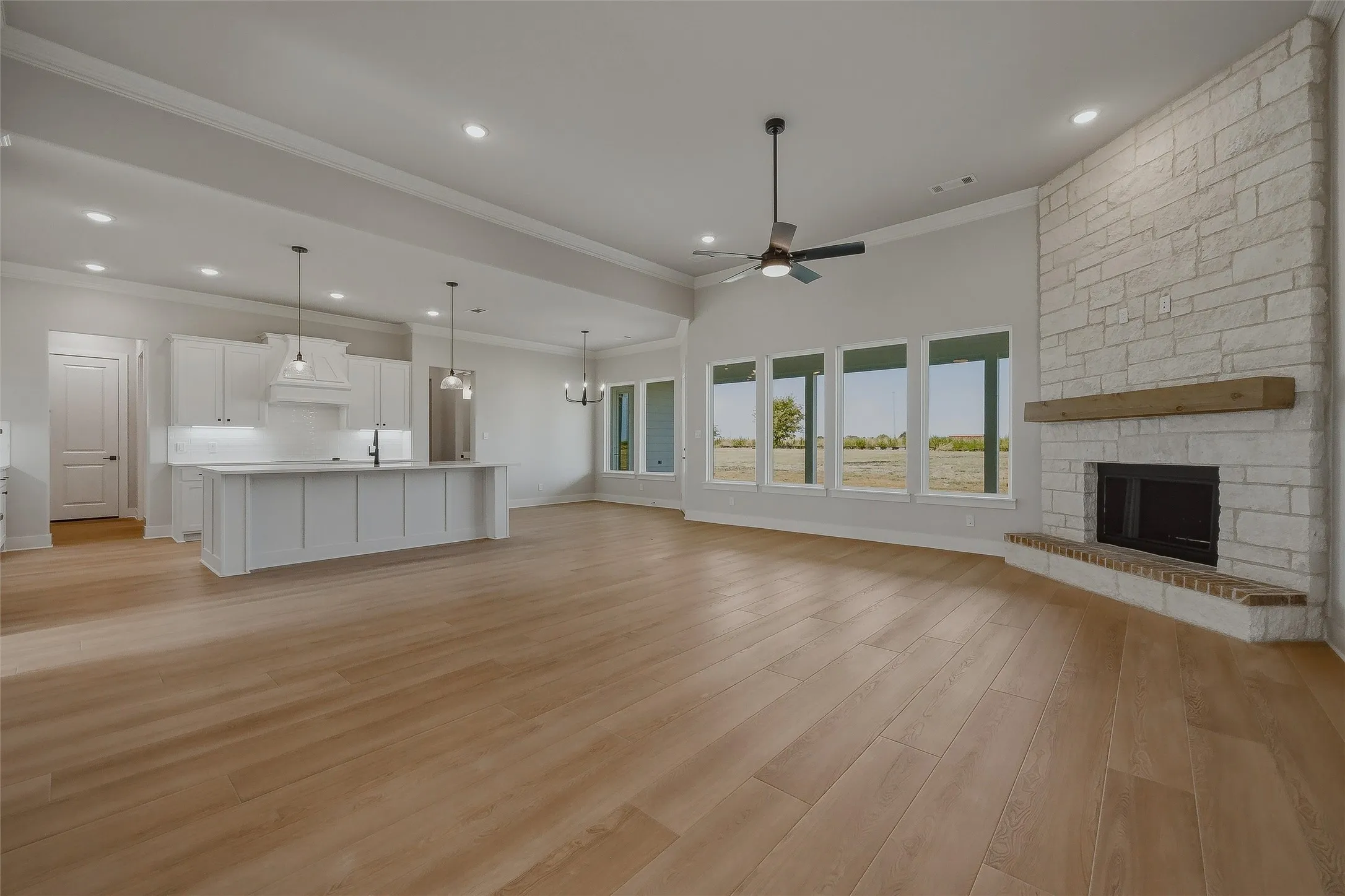 Open-concept living space featuring wood-finish flooring, a stone fireplace with a wood mantle, and multiple windows