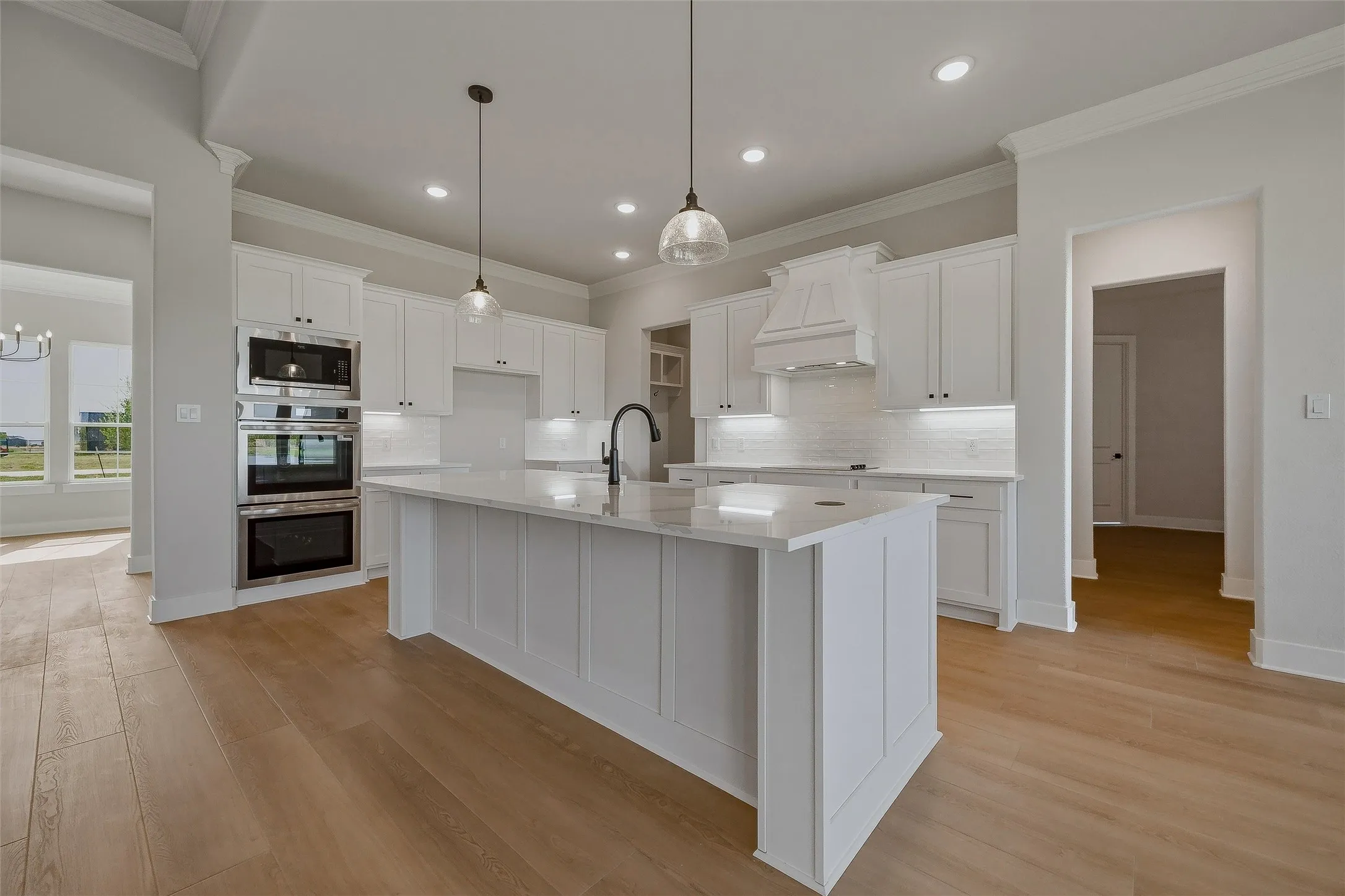 Gourmet kitchen with wood-finish flooring, white cabinetry, a center island with a sink, and stainless steel double ovens