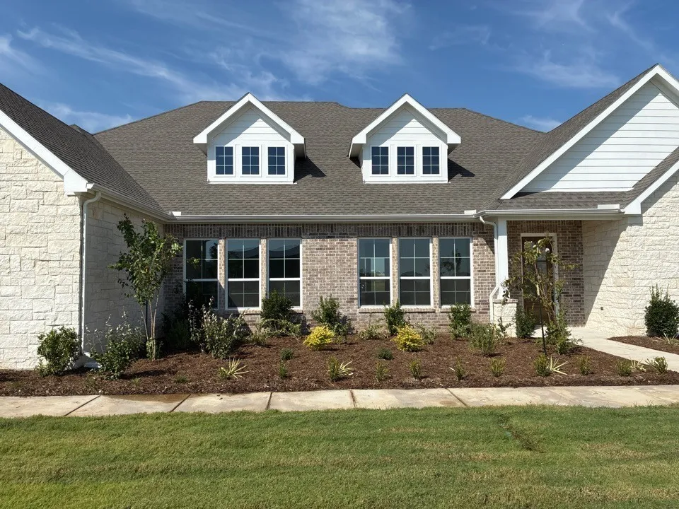 Exterior featuring a stone and brick facade, multiple dormer windows, a covered entry, and a landscaped planting bed