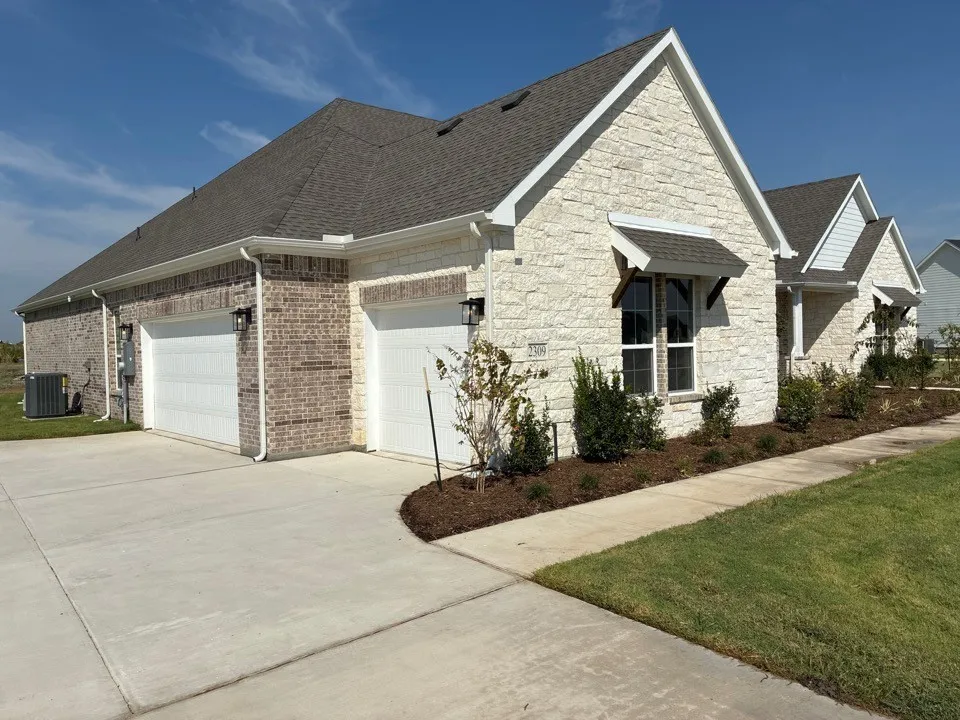 Exterior featuring a combination of brick and stone facade, dual garage doors, a concrete driveway, and established landscaping with a sidewalk